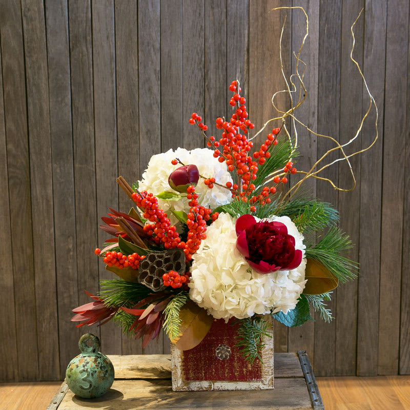 Holiday Cheer- Designer's Choice - This fun winter arrangement is a great way to show someone you're thinking of them this holiday season. Designed in whites and reds, with berries and pine, they'll know you're sending warm winter wishes! While flower availability is subject to change, and may differ from that shown, your arrangement will be designed in a similar style and feel to that shown. Container will be different from that pictured.