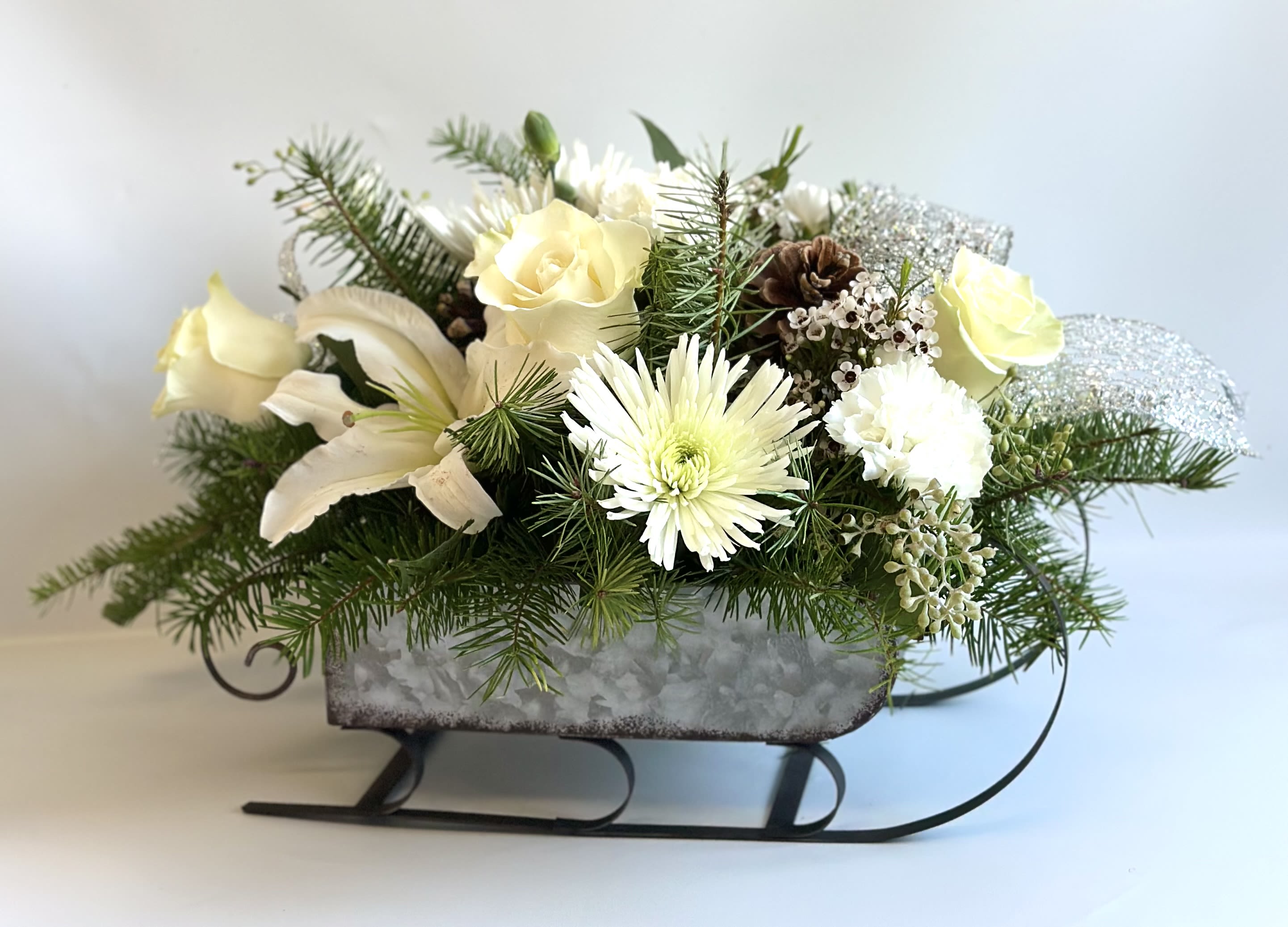 Winter Wonderland Sleigh by Barb’s Flowers - This large metal sleigh is a perfect keepsake for every Christmas to come, filled with Lilies, roses, spider mum, carnations, pinecones and touches of silver ribbon. 