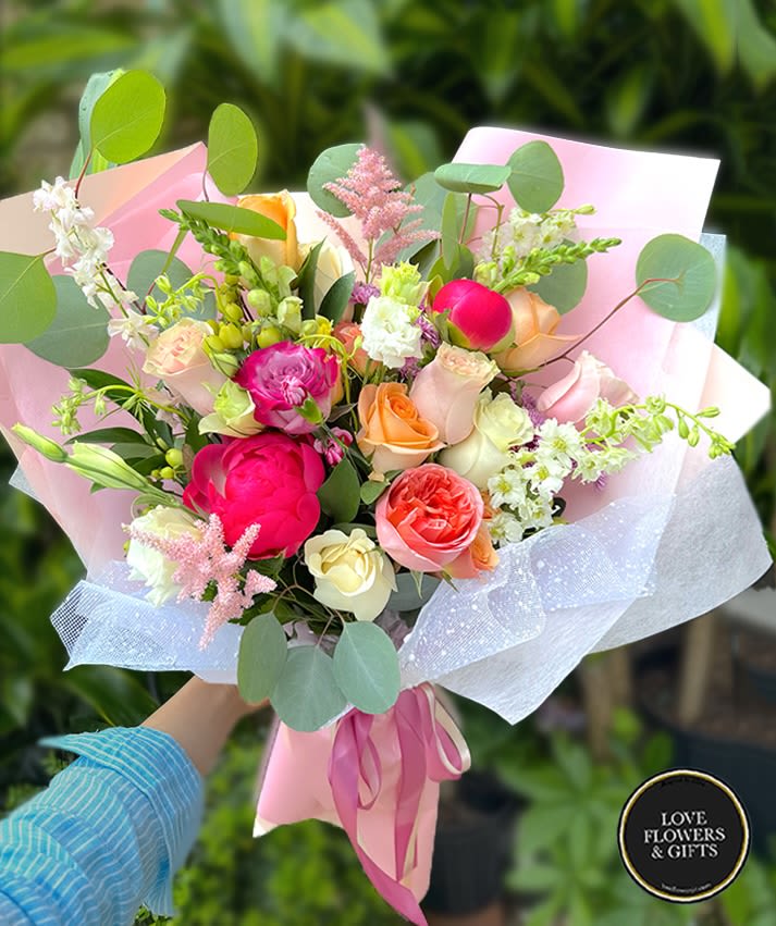 Hand-tied bouquet of pink peonies and mixed roses wrapped in pink paper with ribbon