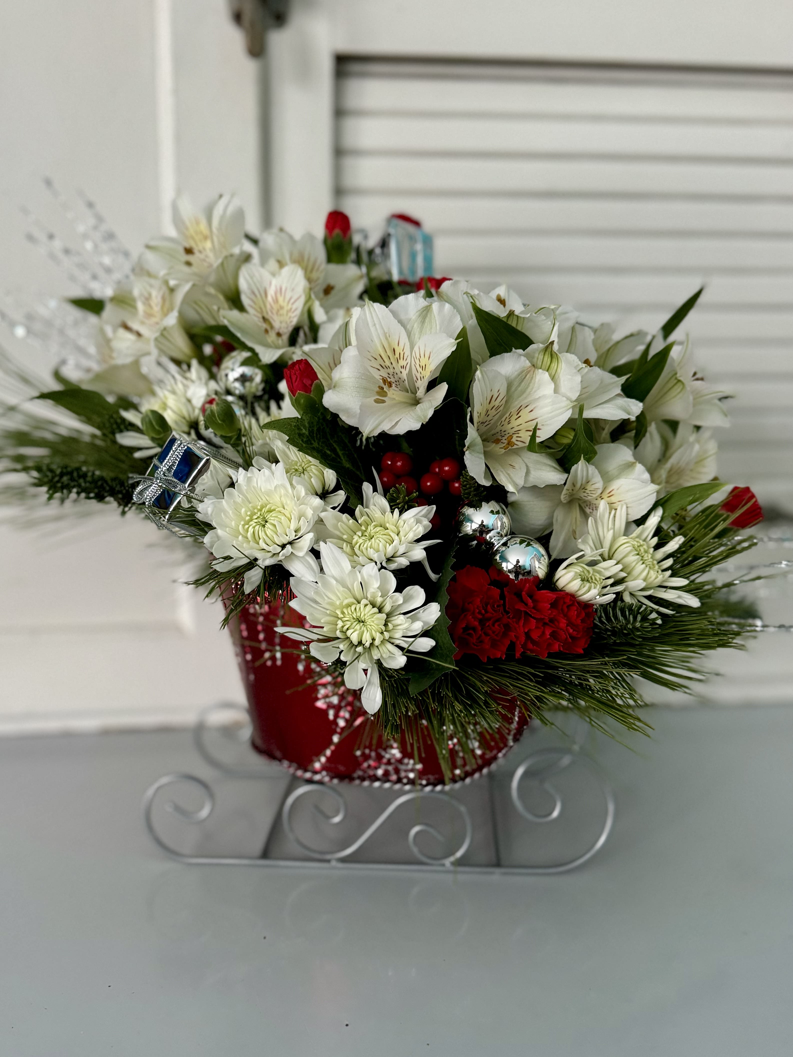 Holiday Sleigh Ride - A vintage-inspired sleigh holds a beautiful mix of flowers, festive ornaments, and evergreen sprigs. This arrangement is a delightful way to bring seasonal charm to any space.
