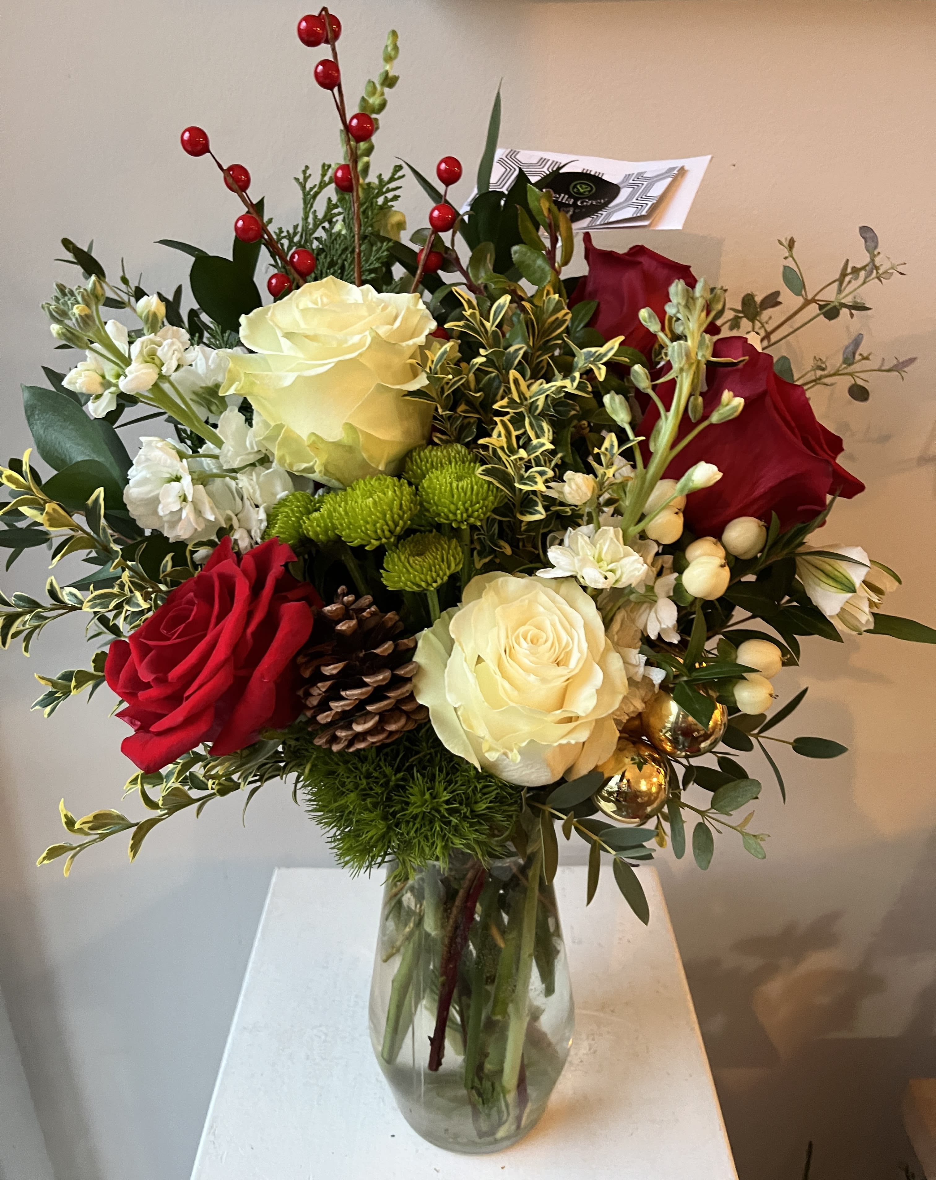 Holiday Cheer  - A Holiday Bouquet with white roses,  red accents, vibrant greens, red berries and evergreen accents and silver or gold bells.