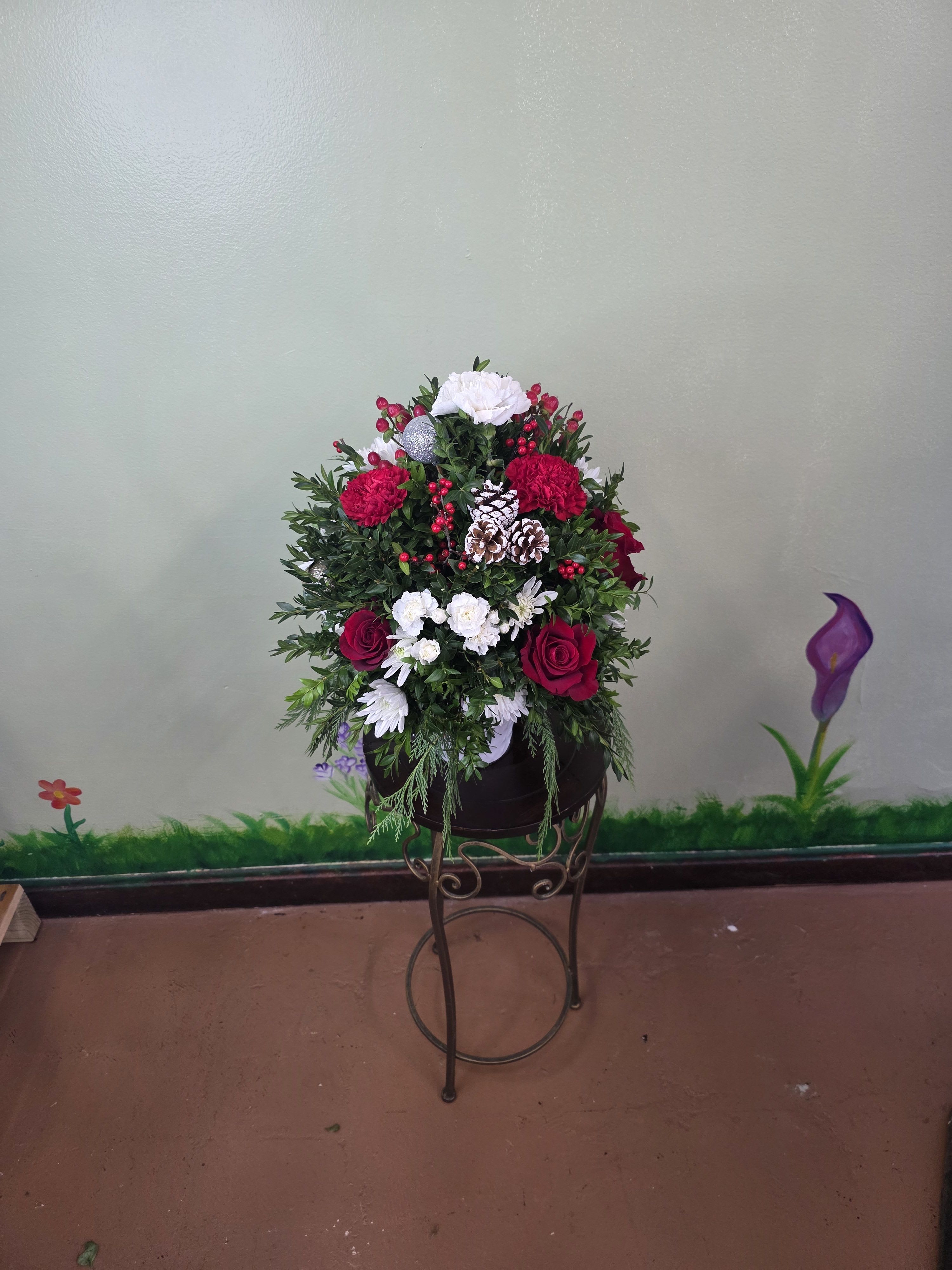 Christmas Cheer Garden - Christmas Cheer Garden is a lush and joyful holiday arrangement featuring vibrant red roses, cheerful white blooms, and rich evergreen foliage. Accented with festive red berries, frosted pinecones, and seasonal greens, this design captures the warmth and magic of Christmas. Arranged in a decorative keepsake container, it’s perfect for spreading holiday cheer on tables, entryways, or as a thoughtful seasonal gift.