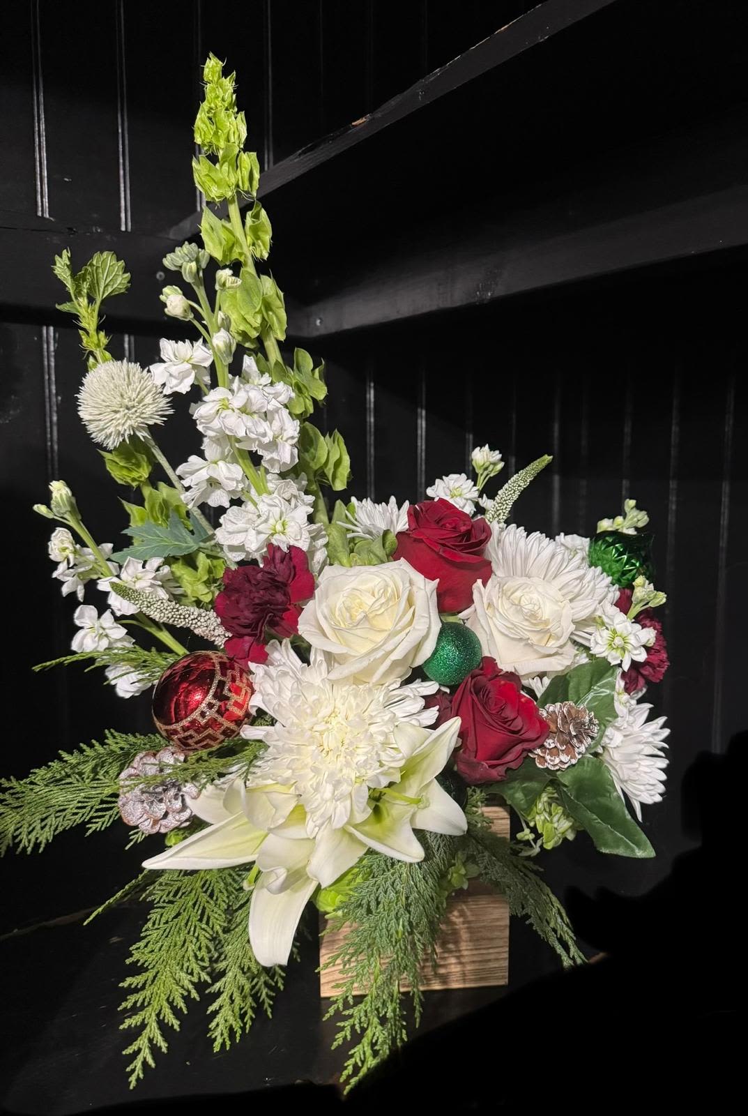 Joly's Quaint Christmas centerpiece. - Bring the spirit of the holiday season indoors with this beautiful arrangement. The beautiful red, white roses and lily's pair gorgeously with the sprigs of pine and pine cones to create a simply stunning rustic mix and ornamental.