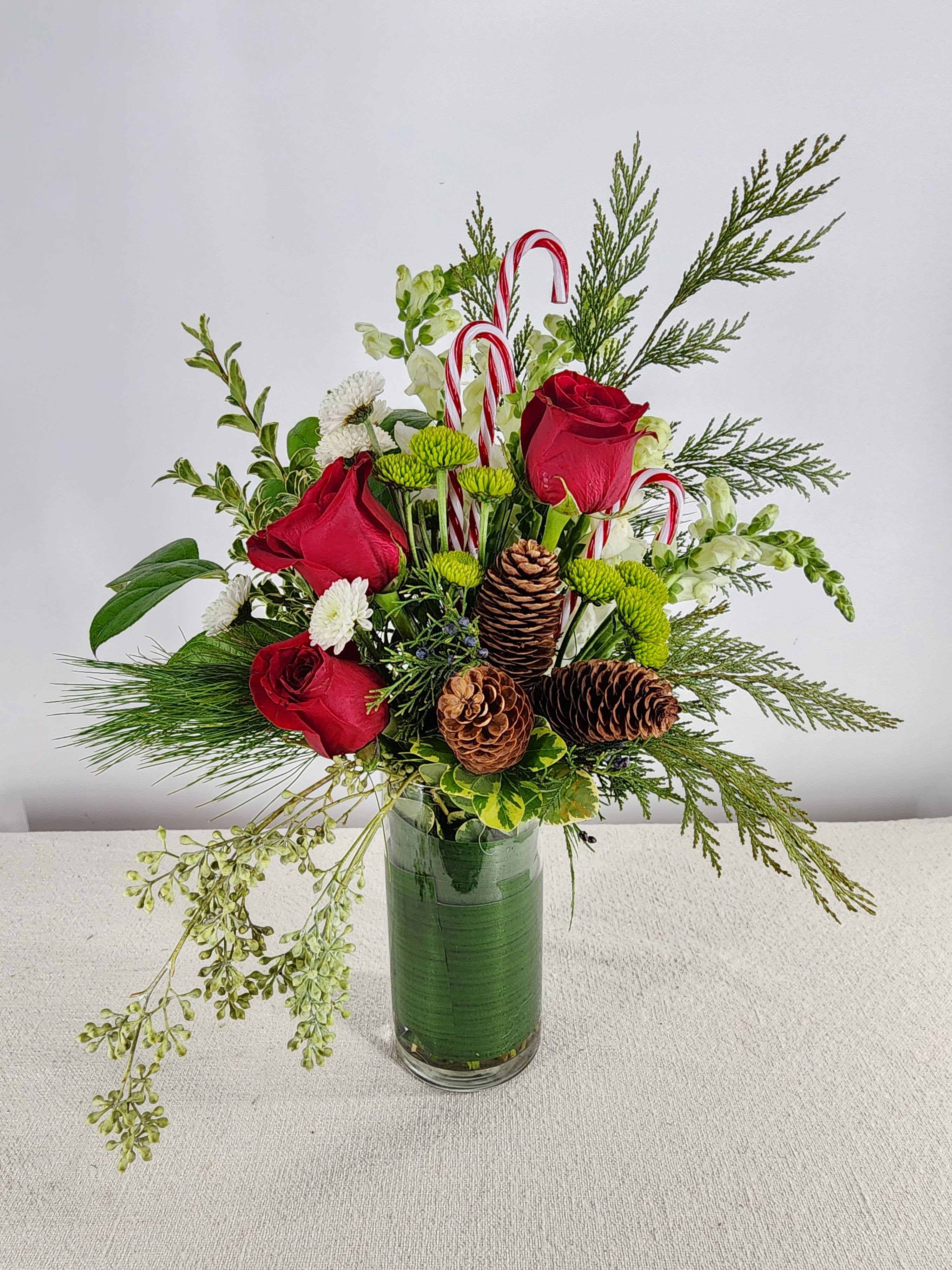 Candy Cane Surprise. - Celebrate the festive season with a delightful arrangement that captures the joy and whimsy of the holidays. This cheerful bouquet combines the classic beauty of vibrant roses with playful candy canes, creating a perfect blend of elegance and charm.