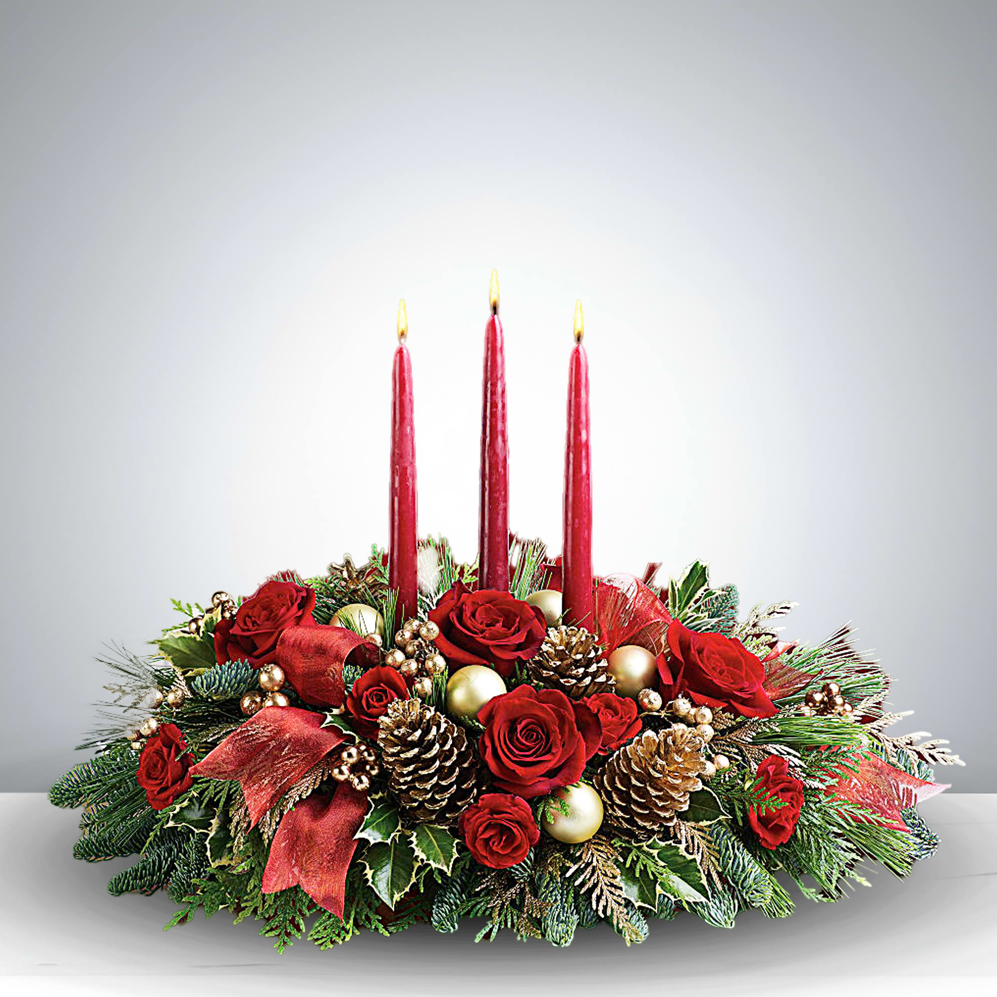 Red Light Christmas Centerpiece - Bring the spirit of the season to life with the Red Light Christmas Centerpiece, a stunning blend of classic holiday charm and refined floral design. At its heart, three glowing red candles rise above a lush bed of crimson roses, pinecones, and golden baubles, surrounded by evergreen sprigs, holly leaves, and festive ribbon accents. This handcrafted arrangement evokes warmth, celebration, and timeless beauty—perfect for Christmas dinners, mantel displays, or holiday gifting. Whether you're creating a cozy ambiance or elevating your seasonal décor, this centerpiece delivers a bold yet graceful statement.