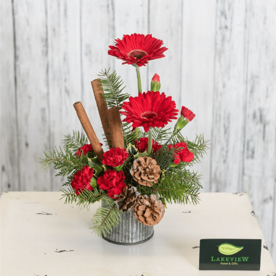 Partridge - A unique way to get into the holiday spirit!  A galvanized steel container with textural greens, bright gerbera daisies, mini carnations and mini pine cones.   Approx: 11"H x 8"W