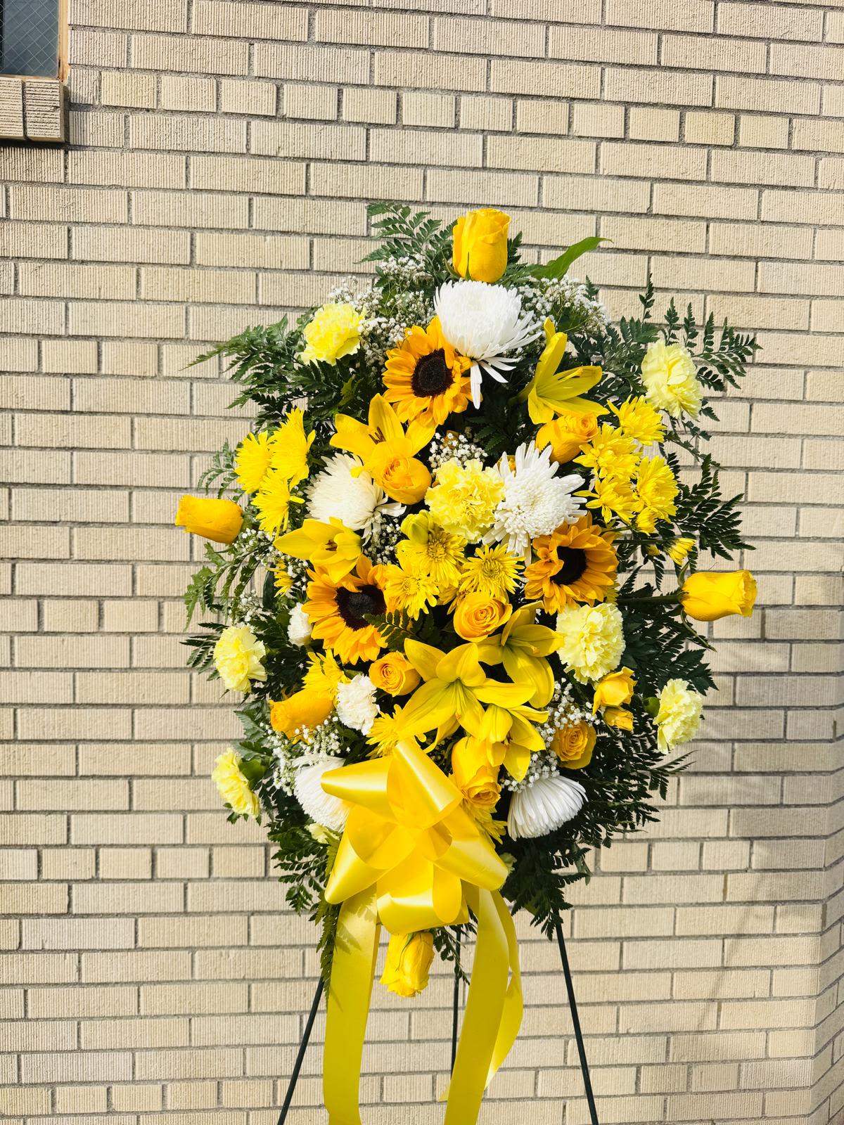 Sunny Memories Standing Spray (small) - Blooming Yellow Standing Spray is a graceful display of sweet serenity. Yellow roses, Asiatic lilies, chrysanthemums, sunflowers and carnations are delicately arranged with emerald palm fronds and other lush greens, this spray is a heartfelt way to honor the life of the deceased.