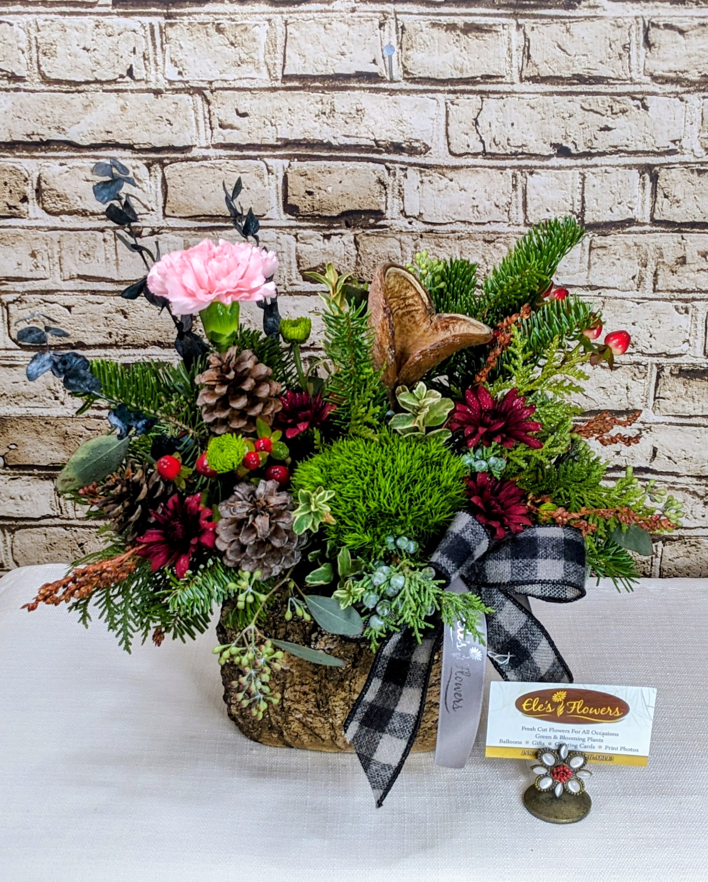 Country Christmas  - Our charming Country Christmas arrangement featuring a delightful blend of burgundy, green, and soft pink flowers that evoke a cozy, rustic elegance. Fragrant evergreens form a lush, festive base, while pinecones add a natural, woodland touch. Perfect for bringing warmth and countryside charm to your holiday décor.  *Blooms may vary.  Approximate Dimension's: 13"H x 16"W