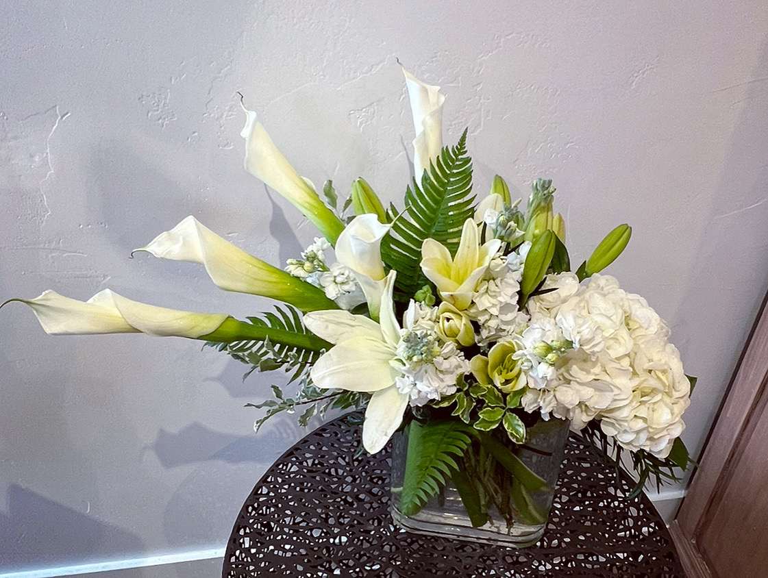 Warm Thoughts - A fresh, crisp design of white calla lilies, hydrangea, asiatic lilies and stock with fresh Chilean greens in an elongated glass vessel.