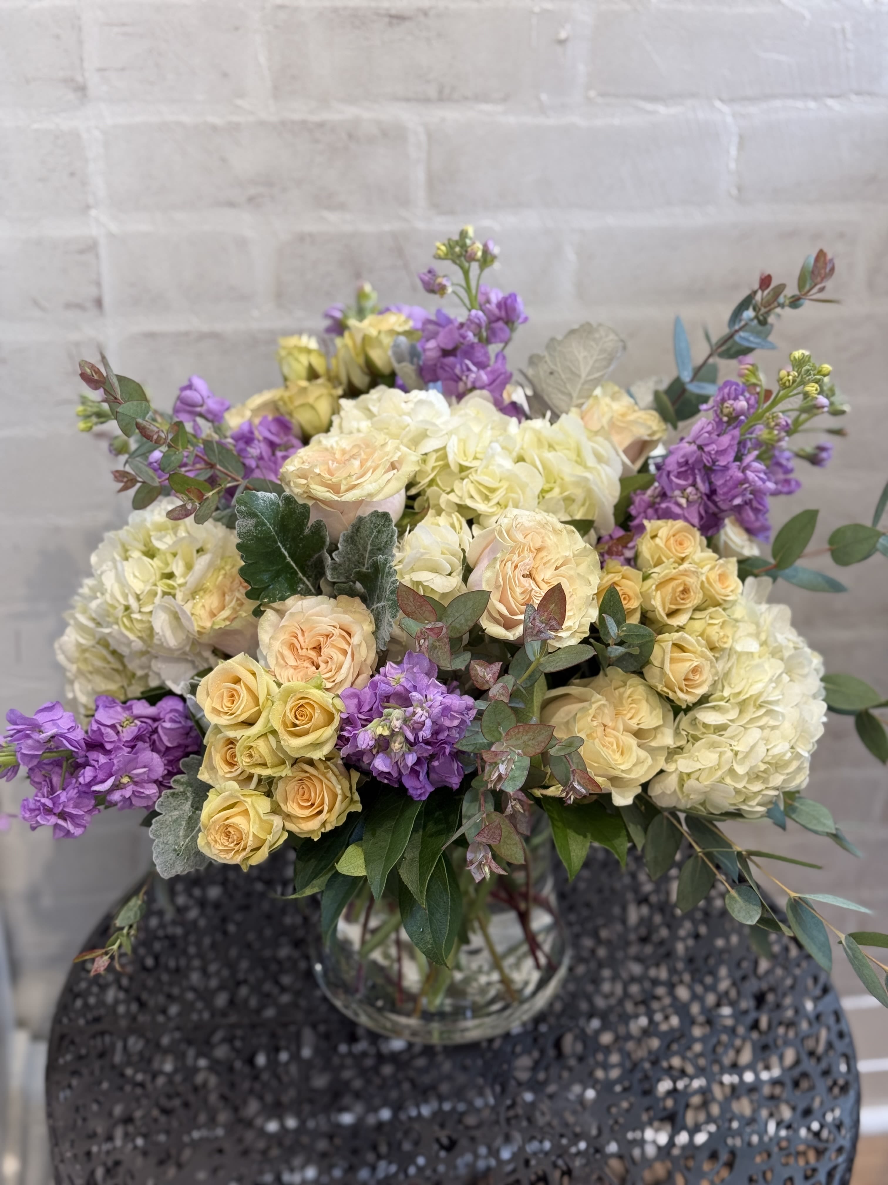 In The Garden - Lush hydrangeas nestled within pastel hued beautiful roses, spray roses, fragrant stock and a touch of fauna. 