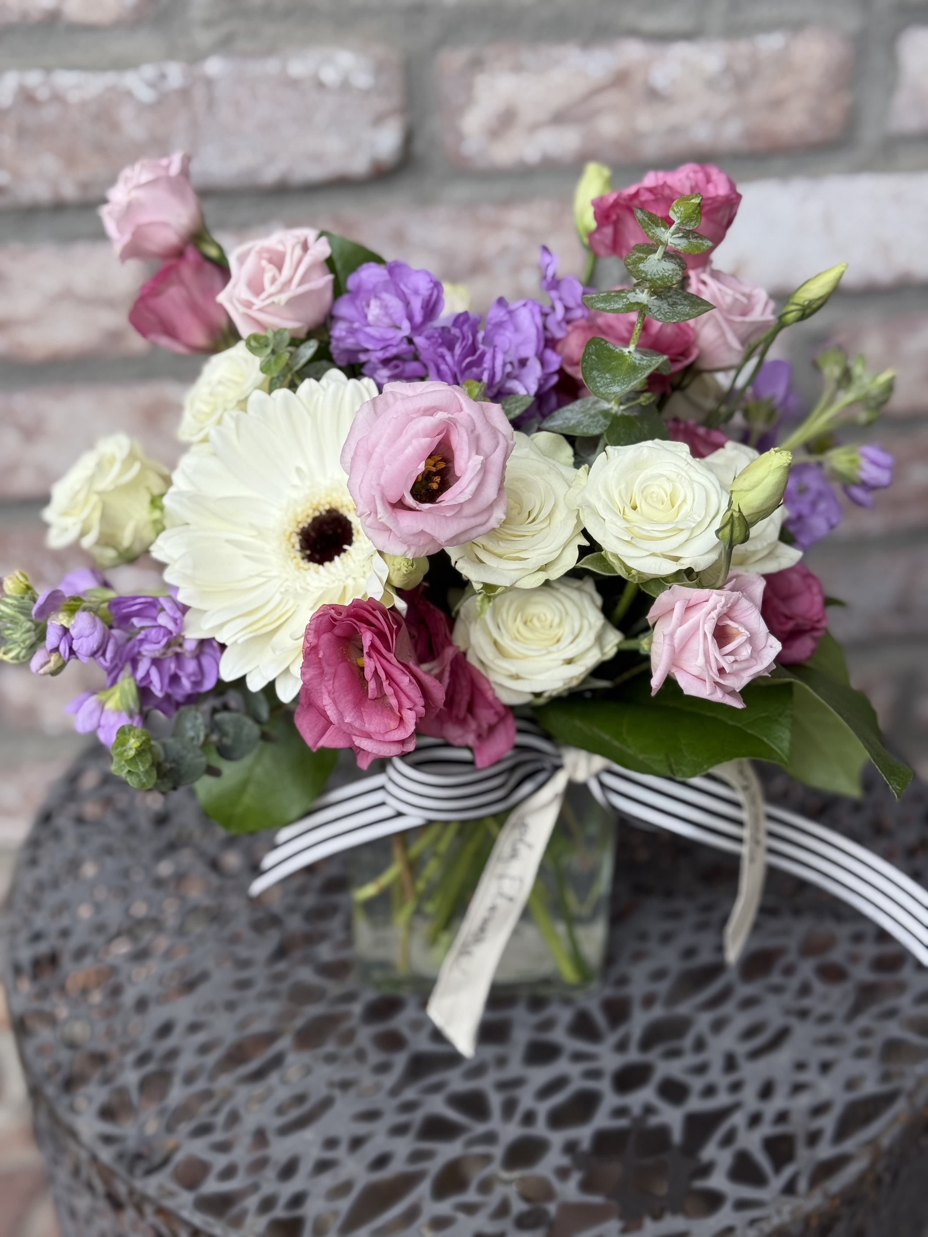 Love You More - A Beautiful, soft design of stock, spray, roses, lisianthus , Gerbera daisies, and fragrant eucalyptus. Designed in a rectangular glass vase. Finished off with our signature ribbon. Perfect for a small statement piece or end table. 