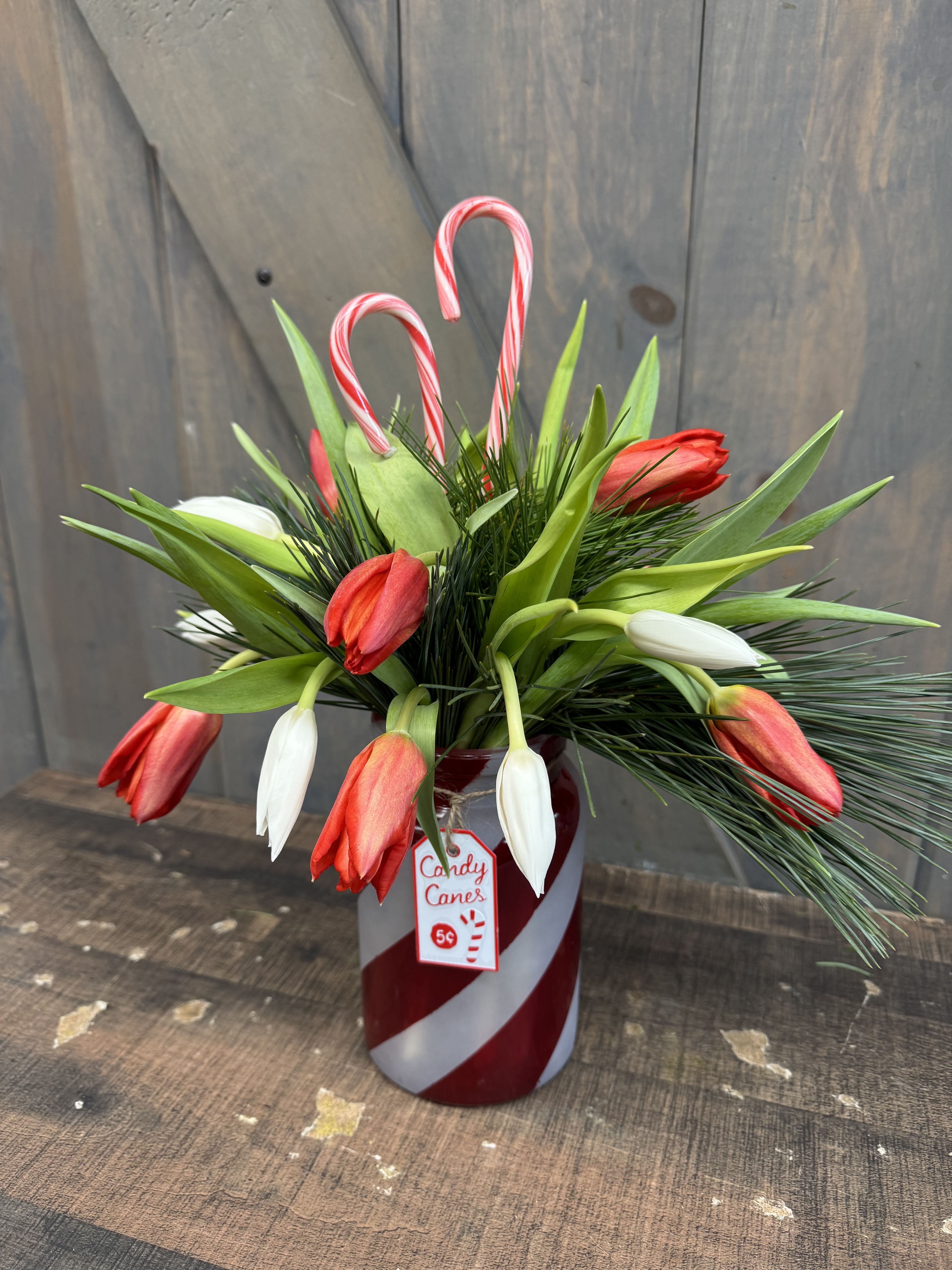 Candy Canes and Tulips - This festive arrangement does a great job of spreading the Christmas Cheer! The flowers arranged in the keepsake candy cane glass vase and 10 White and 10 Red Tulips with mixed winter greens and 2 candy canes!