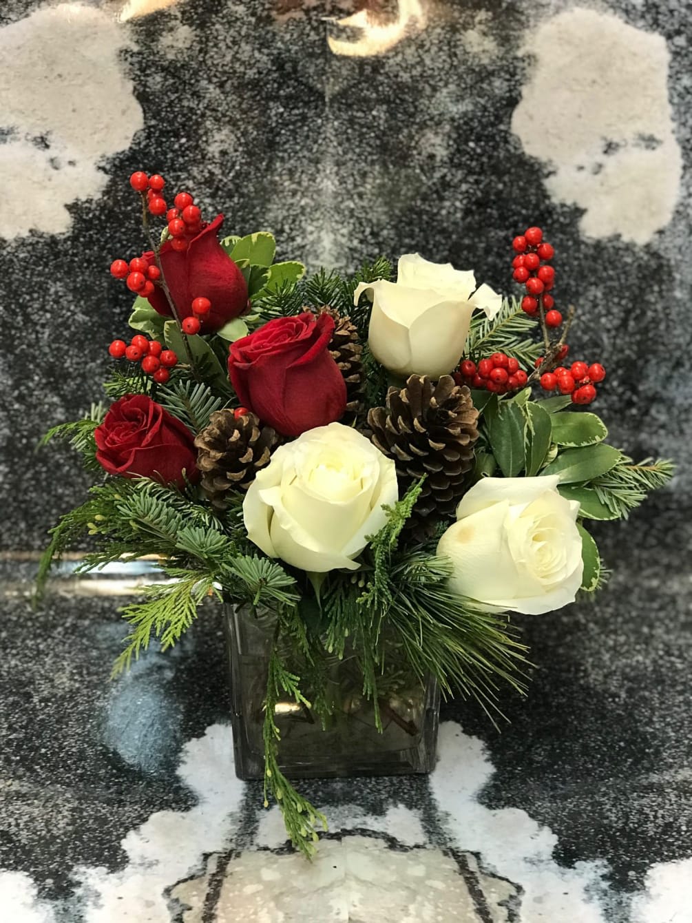 Christmas Wishes Cube Vase Arr - Festive Christmas Greens Designed in a contemporary cube vase with Red and Creme White Roses Berries and Pine Cones 