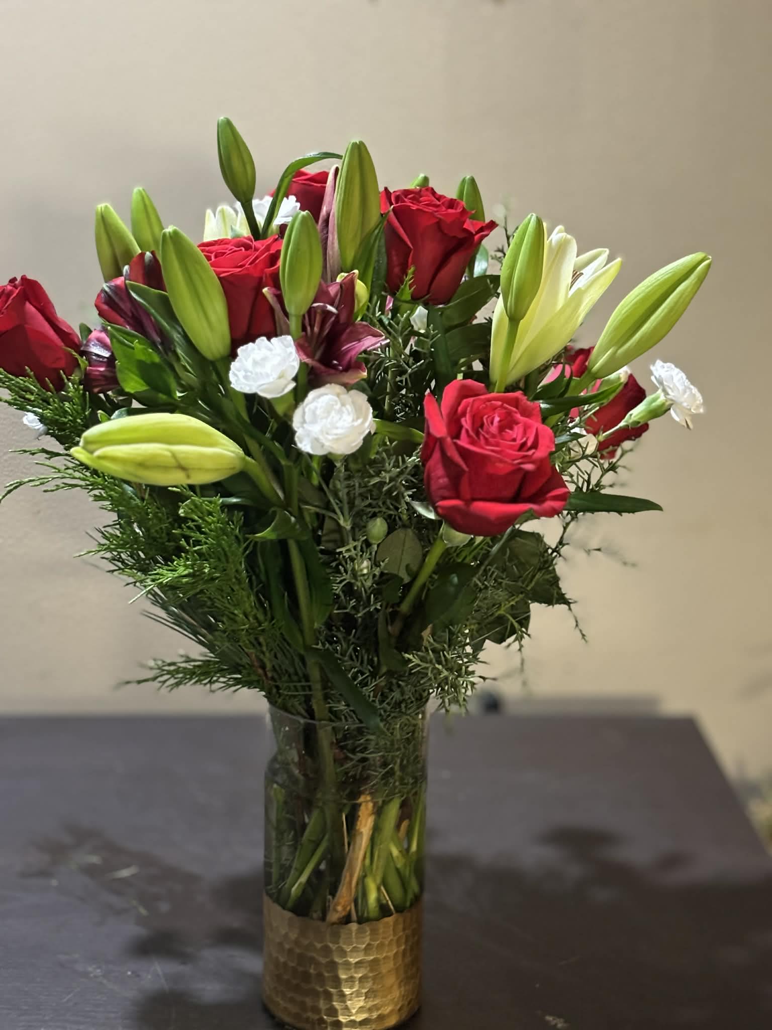 Rose &amp; Lily Delight - This stunning floral arrangement features lush roses and graceful lilies, beautifully accented with fresh pine tree greens and delicate small white flowers. Designed in a luxurious gold-dipped vase, the combination of soft blooms and rich greenery creates a timeless and elegant look. Perfect for celebrations, sympathy, or adding a touch of refined beauty to any space.