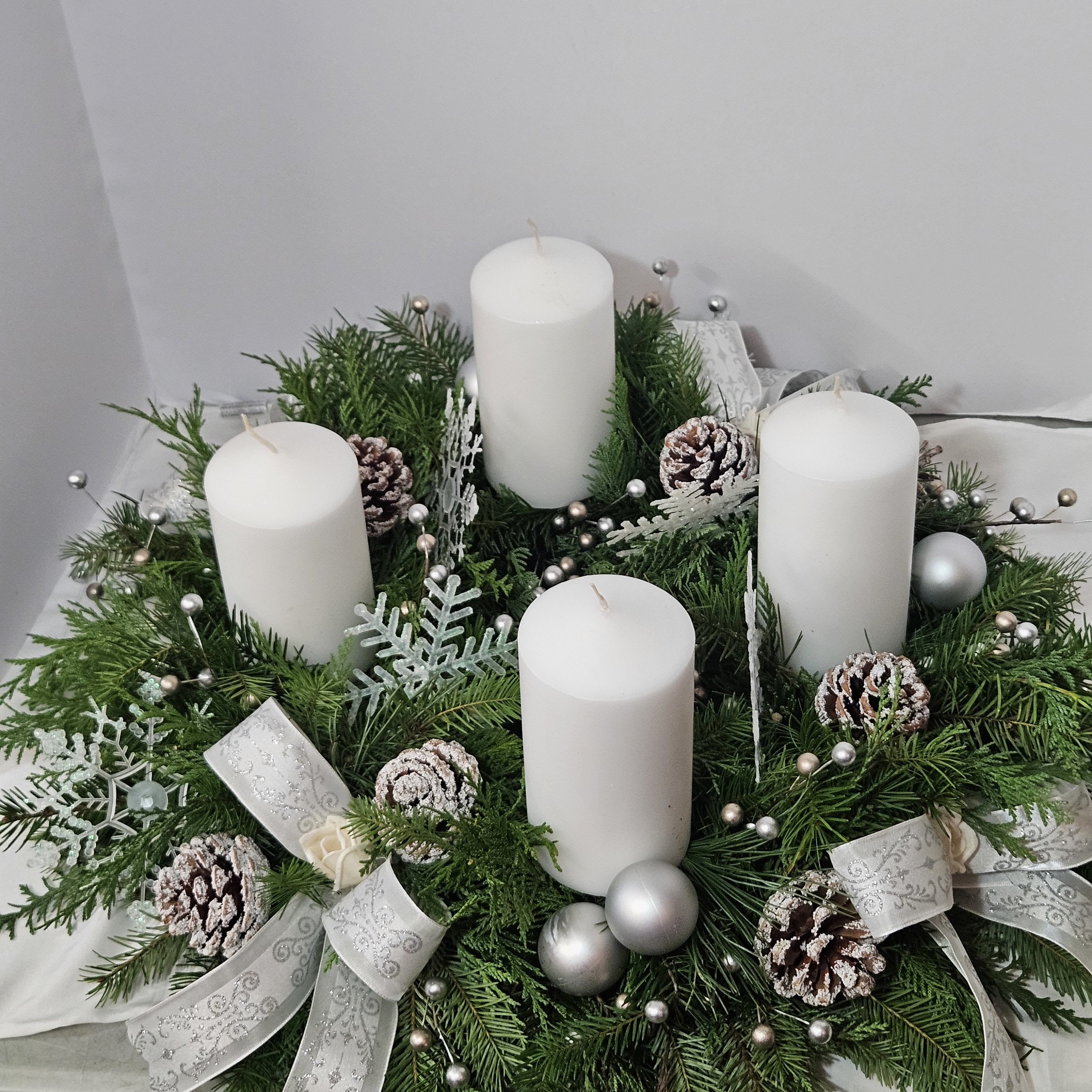 SILENT NIGHT CENTETPIECE - *Can be Round or Longated* A beautifully created fresh evergreen centetoiece adorned with christmas decore and beautiful white candles.  Each piece is individually created so product may vary. Standard - 1 candle, Deluxe - 2 candles,  Premium - 4 candles