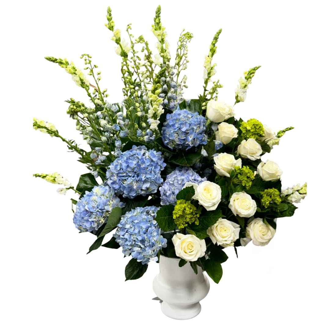 Cloud Nine XL - A big, airy statement arrangement featuring blue hydrangeas, creamy white roses, and tall delphinium for that elegant “height + drama,” finished with lush greens in a classic white urn. Fresh, clean, and super upscale, perfect for events, entrances, and major moments.