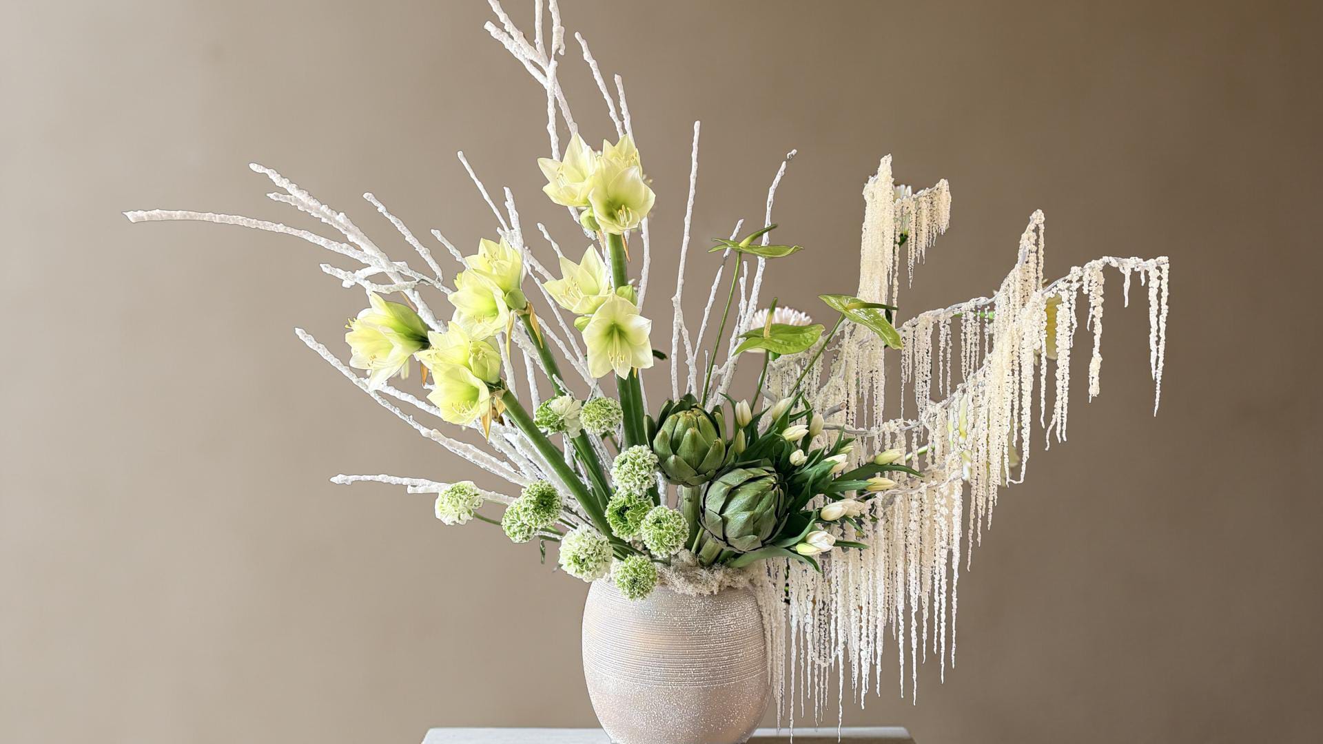 Lumiere d'Hiver - A modern winter statement designed to captivate. Winter Whisper Elegance blends soft ivory blooms with sculptural textures and frosted branches, evoking the quiet beauty of a winter morning. This arrangement brings sophistication, calm, and timeless charm—perfect for luxury homes, winter celebrations, hotel lobbies, and elegant events.