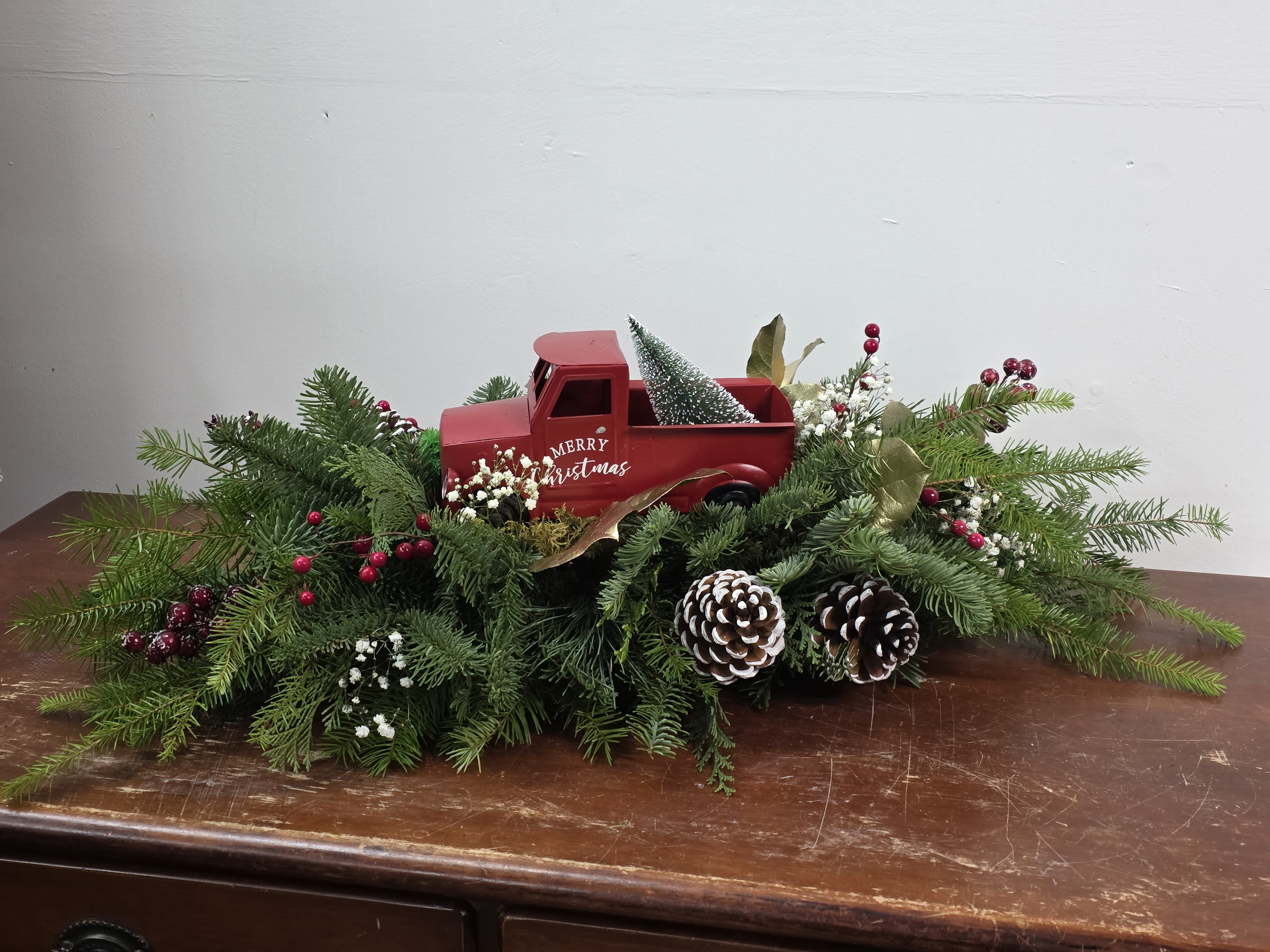 Grandpa's Truck - Adorable keepsake tin truck tucked among evergreens, pine cones and babies breath. Long lasting, fragrant, and a great piece for a long table, sofa table or credenza. Upgrade to deluxe and we add beautiful red carnations. Upgrade to premium and we add red carnations and roses for a truly beautiful and unique gift. 