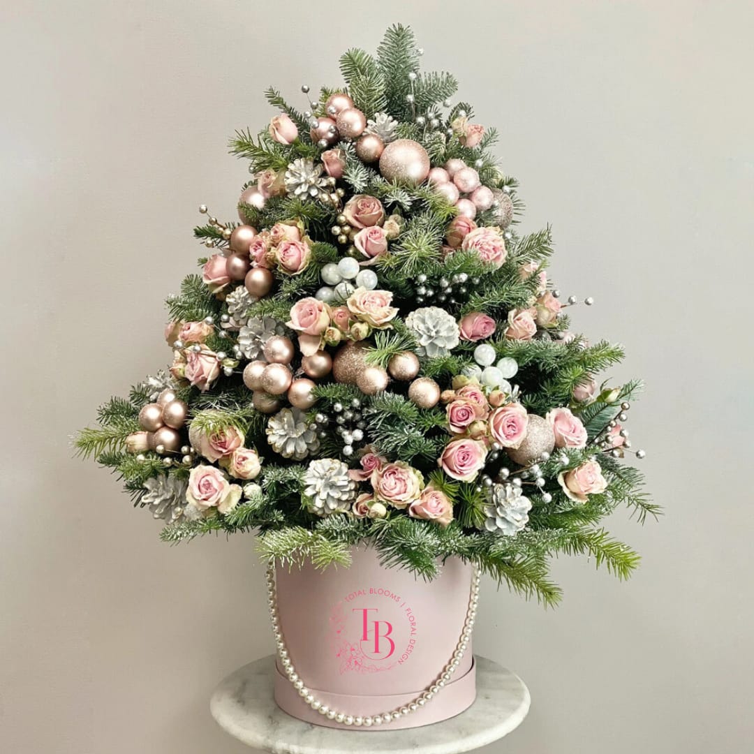 Rose De Noel Holiday Tree - Pink, white, and champagne tones are brought together in our stunning Christmas tree composition which consists of baby roses, Christmas tree leaves, pine cones, and holiday decor.  DISCLAIMER: THIS TREE IS MADE OF FRESH CUT FLOWERS AND DOES NOT HAVE A LIFE EXPECTANCY OF A NATURAL CHRISTMAS TREE. THE BRANCHES ARE CUT STEMS AND PLACED INTO FLORAL FOAM. 