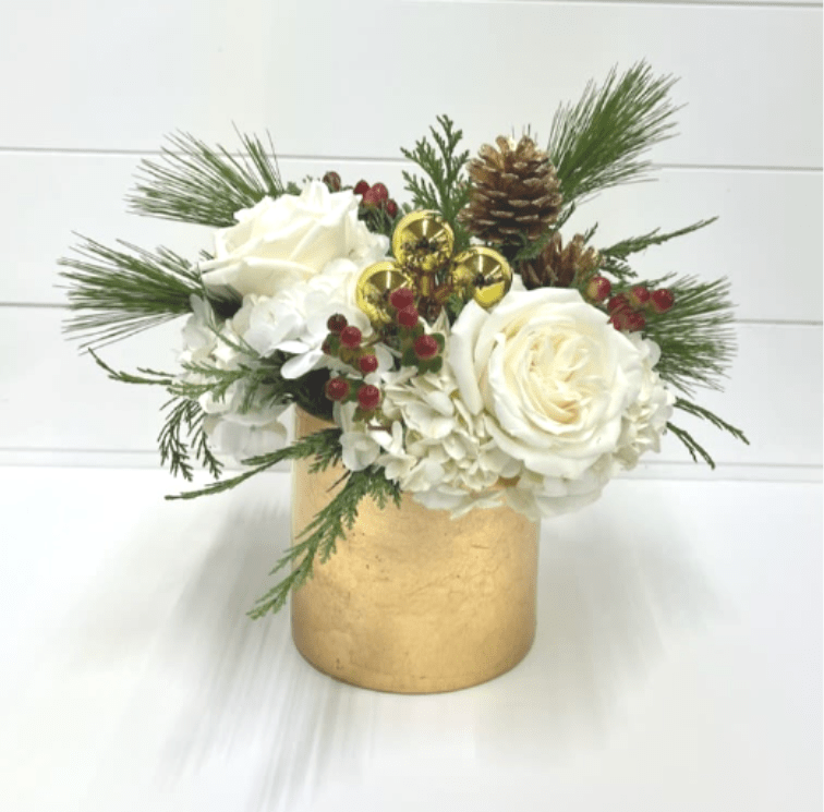 Rich and Merry - Elegant holiday floral arrangement featuring white roses and hydrangeas, accented with winter greens, pinecones, red berries, and gold ornaments. Designed in a modern gold cylinder vase, this festive piece makes a beautiful statement for holiday décor, centerpieces, or seasonal gifting.