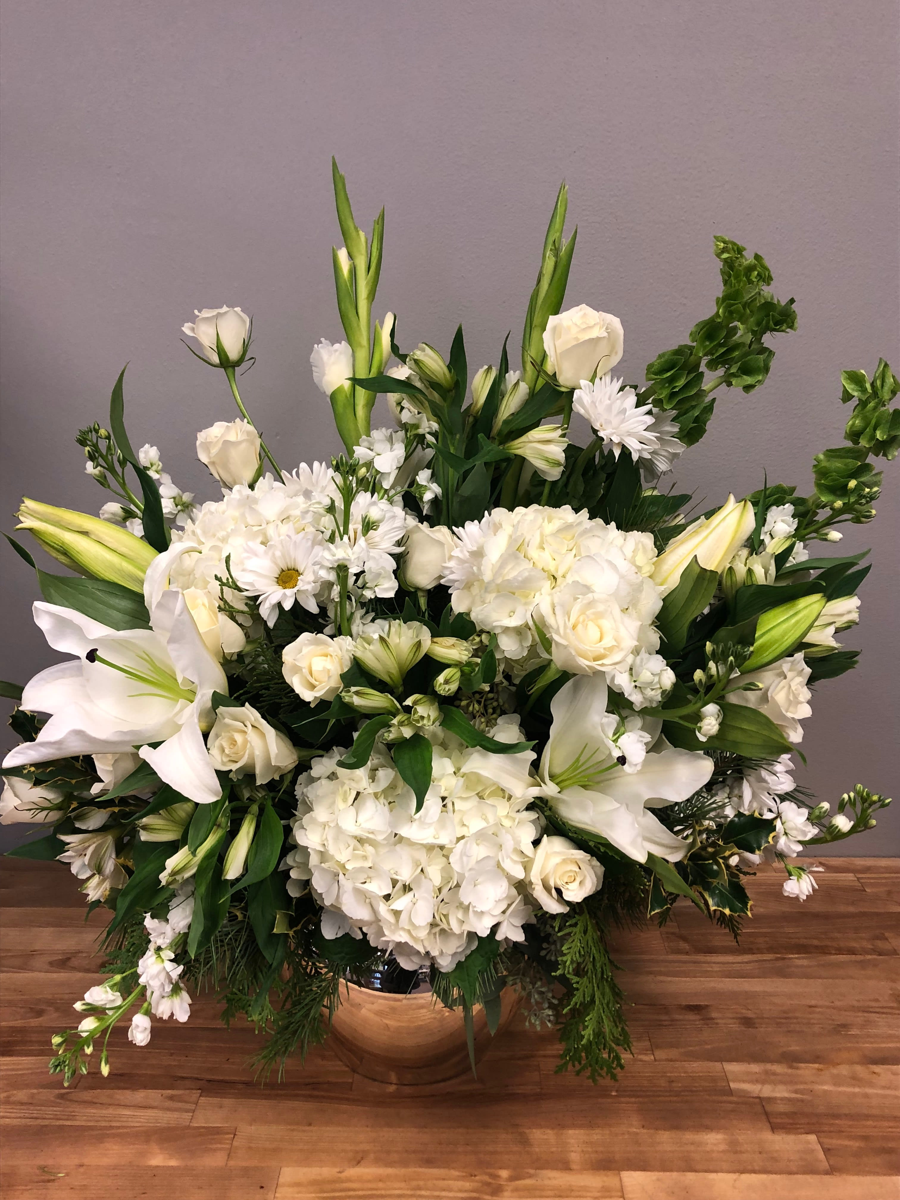 Grand White Flower Selection - Full of assorted white flowers, accented with beautiful greens. Seasonal blooms and greens allow for this arrangement to maintain a classic yet up to date look throughout the year. The standard design is quite large, and the deluxe and premium upgrades are even more grandly sized.  Perfect for a front foyer or a large sympathy arrangement. 