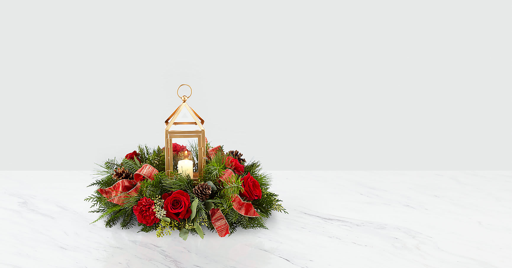 Beautifully Bright™ Centerpiece - The Beautifully Bright Centerpiece draws in the attention of the room while perfectly accenting the holiday festivities. An array of red roses, red carnations, seeded eucalyptus and Christmas greens make up a truly wonderful arrangement. Whether it's a gift for you or someone else, this piece clearly belongs in the center of the room. A candle shines within the glass insert surrounded by a matte gold metal lantern.  ITEM #18-C3S