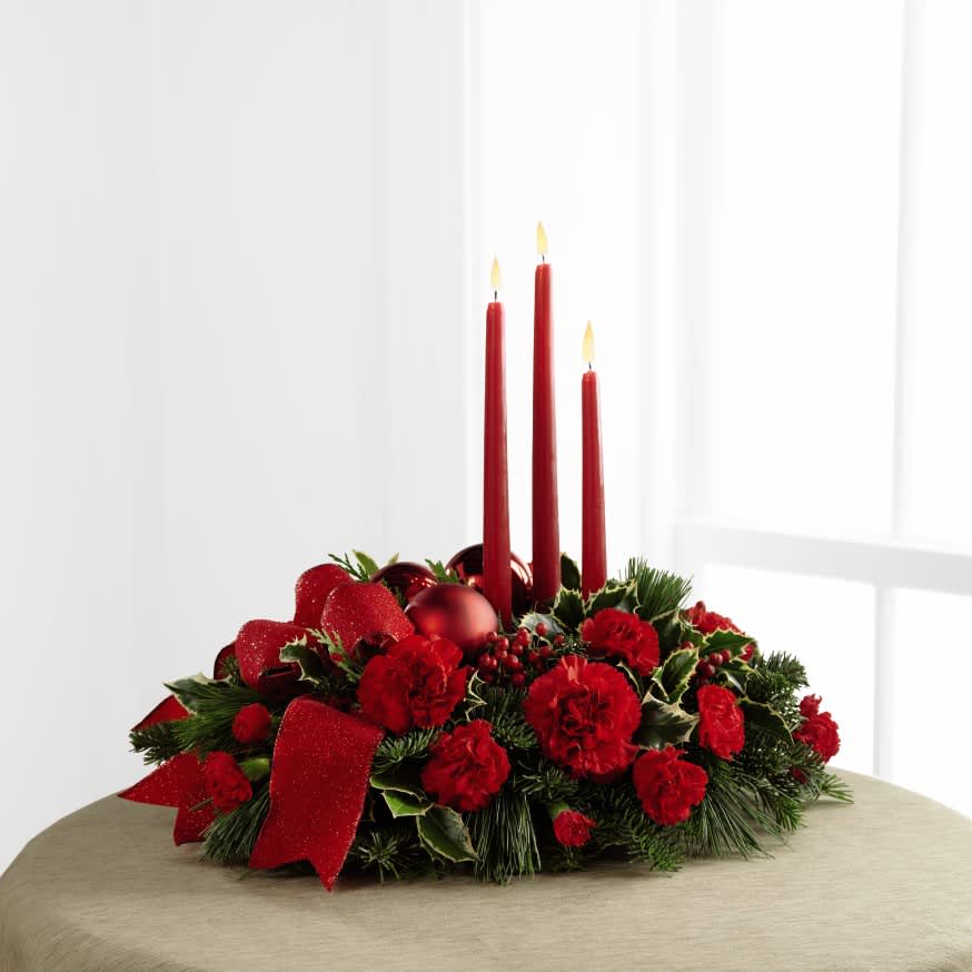 The FTD® Lights of the Season™ Centerpiece - The FTD® Lights of the Season™ Centerpiece is an exquisite way to bring the magic of the holiday season to your celebrations with family and friends. Brilliant red carnations and mini carnations are gorgeously arranged amongst variegated holly and an assortment of holiday greens. Accented with red glass balls and a bright red wired ribbon, this arrangement encircles 3 red taper candles to bring the perfect glow to your festivities. 