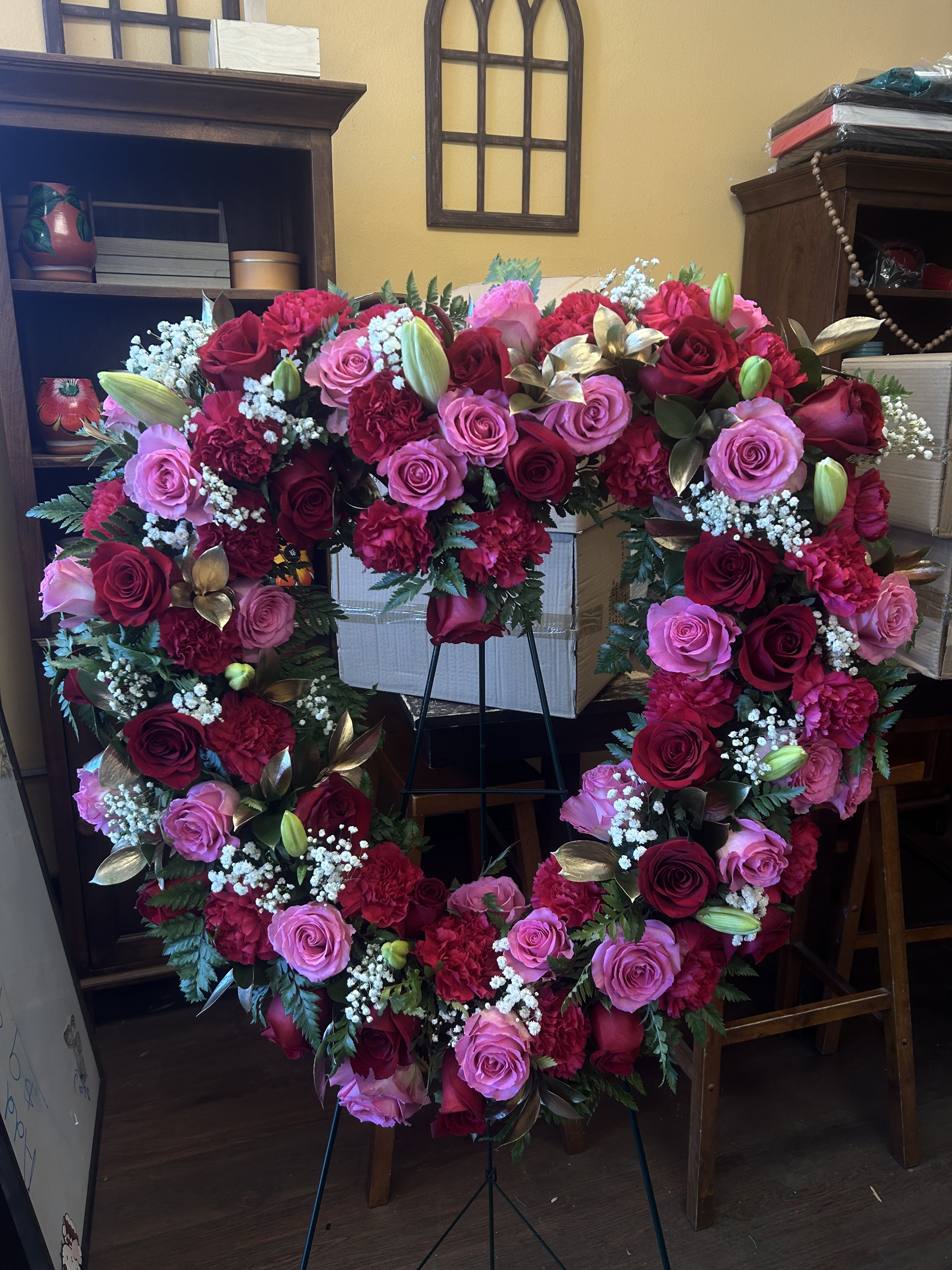 PINK AND RED HEART  - HEART WITH STAND TO INCLUDE PINK AND RED ROSES, PINK AND RED CARNATIONS AND PINK LILES (UNOPENED) AND FILLERS SUCH AS BABY BREATH AND GOLD RUSCUS  PICTURE SHOWN IS DELUXE STANDARD SIZE IS 18 INCHES DELUXE SIZE IS 22 INCHES  PREMIUM SIZE IS ALSO 22 INCHES BUT WE WILL ADD MORE ROSES TO THE ARRANGEMENT 
