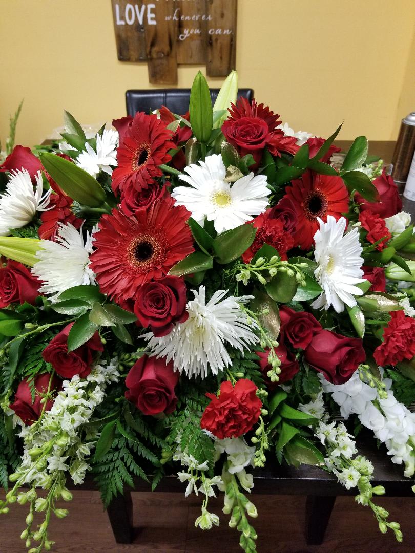 Casket RED LOVE - 24 Red Roses, Red Gerbera Daisies, white Spider Mums, white and red carnations and other fillers.  (NOTE on casket sprays we require at least 2 day notice, to guarantee the same flowers in the picture, if you need it in less than 24 hours it is possible with minor substitutions.  PLEASE CALL US IF YOU HAVE QUESTIONS   Casket size is about 32 inches long and about 20 inches wide 