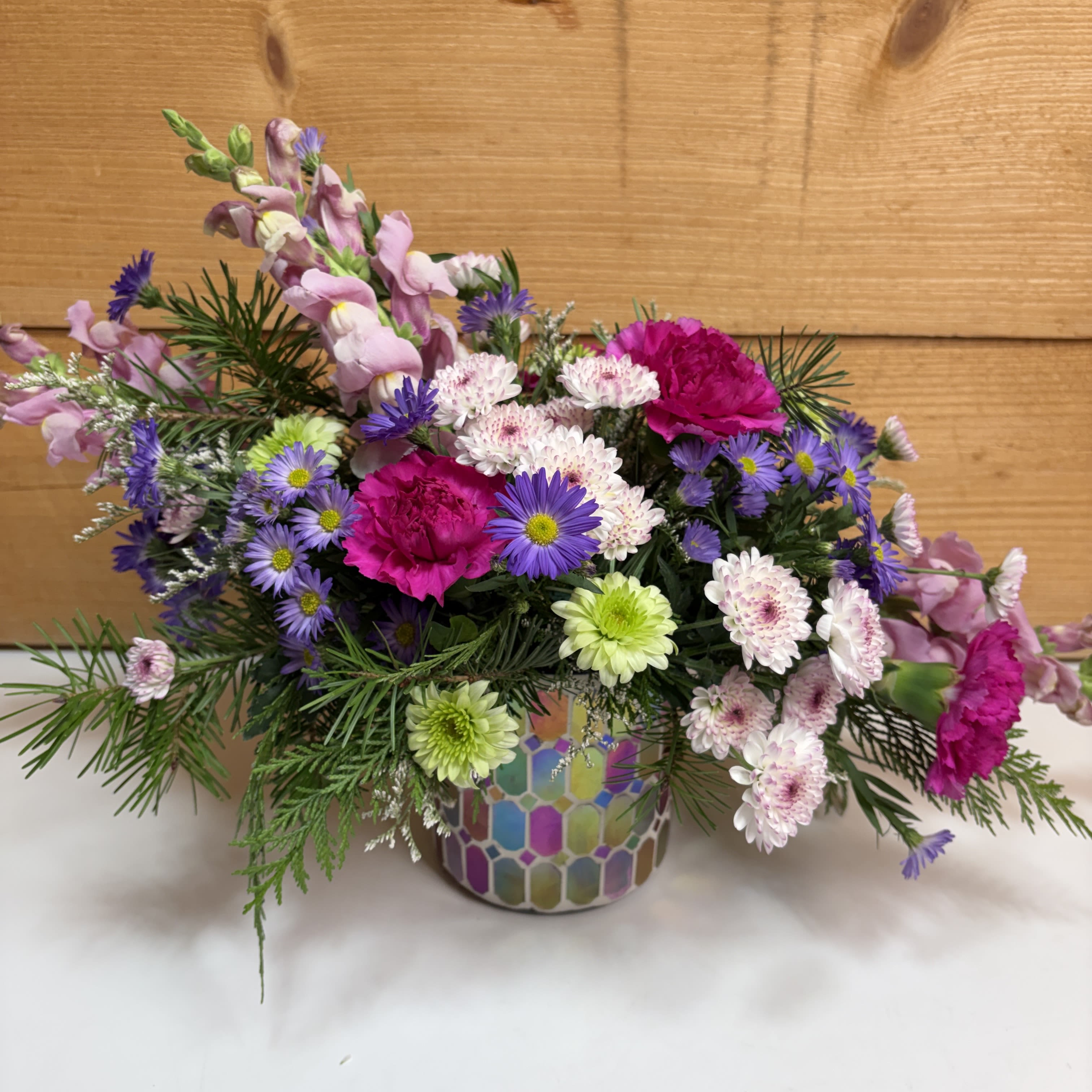 Sugar Plum Whispers - Our Sugar Plum Whispers is proof that this time of year doesn't have to be only red and green! Designed in a colorful mosaic container, this arrangement features various flowers in shades of purple and pink, making this a fun and exciting way to celebrate the season! 