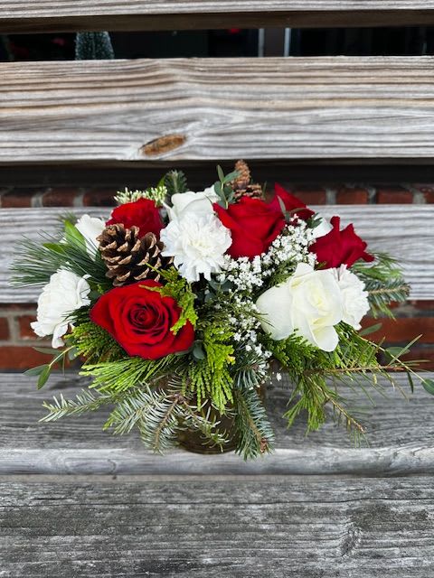 Peppermint Bark - Red and White flowers arranged in evergreens, with touches of pinecones. Clear glass vase. 