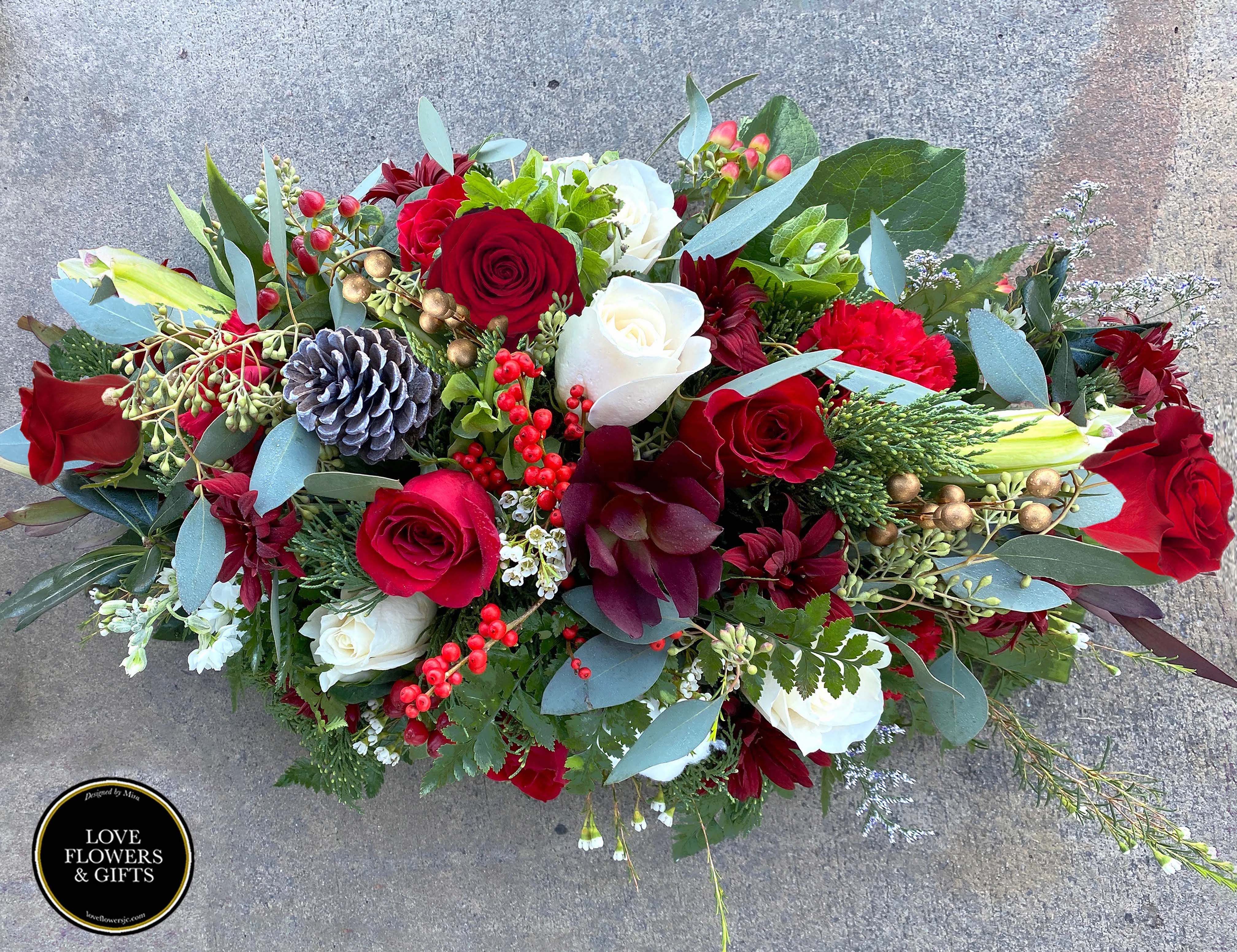 Christmas Classics (Centerpiece) - A beautiful low and wide holiday centerpiece of classic colors and style of white and reds in a bed of fresh holiday greens. Great gift for holiday dinners and gatherings.   Measures appx: 21" by 12" 