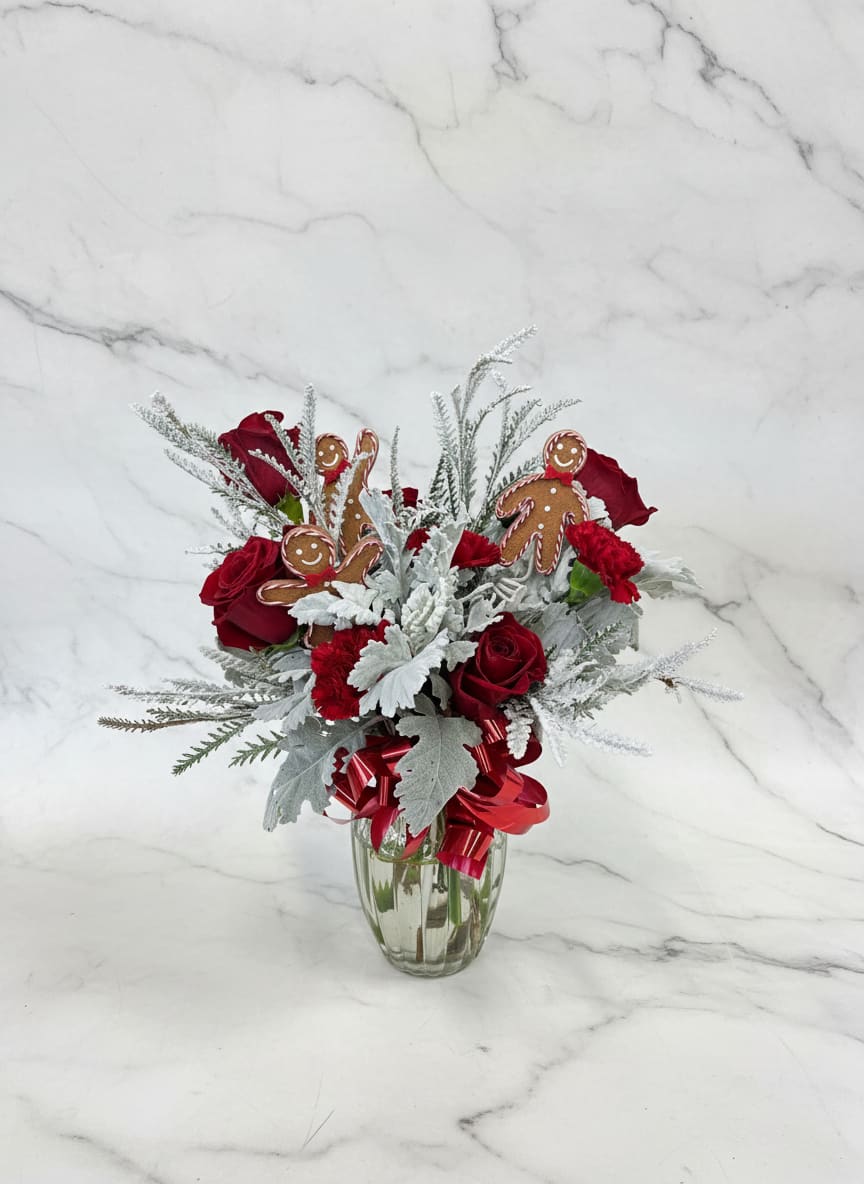 Frosted gingerbread vase - A winter-forward floral design combining classic red roses, soft dusty miller, and flocked evergreens. Gingerbread details add warmth and whimsy, creating a festive arrangement that feels both timeless and inviting.
