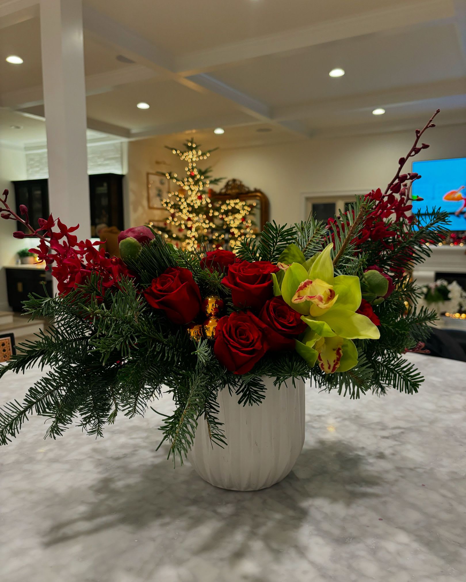 A Little Holiday Cheer - She's festive, she's fun and she's the perfect gift, or home decor accent for the kitchen or coffee table. Roses, assorted orchids, ornaments and holiday greens in a beautiful white ceramic vessel. 