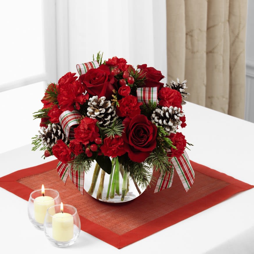 FTD Christmas Coziness Basket - Adding warmth and a homespun look to your Christmas dŽcor, this fresh and fragrant floral arrangement is a wonderful way to bring color and life to any corner of the home. An assortment of Christmas greens and variegated holly are arranged to perfection in a rectangular stained woodchip basket, accented with clusters of red berries, natural pinecones, and a festive red plaid ribbon. A wonderful holiday gift for your relatives, neighbors, or friends throughout the yuletide season ahead. 