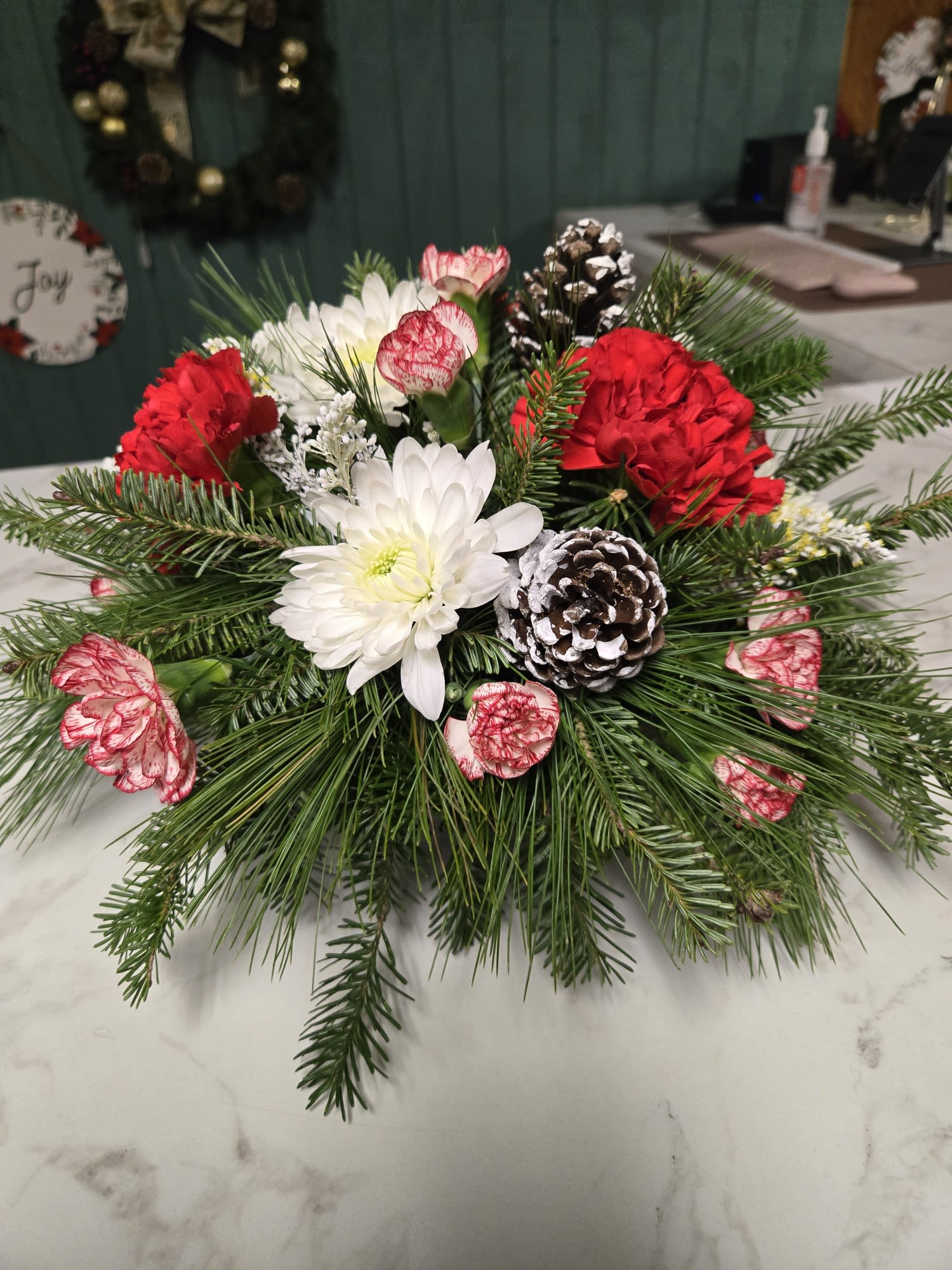 Christmas Centerpiece - Add a touch of seasonal beauty to the holidays. Centerpiece is winter greens, with red carnations, peppermint carnations, white mums, and pinecones. 