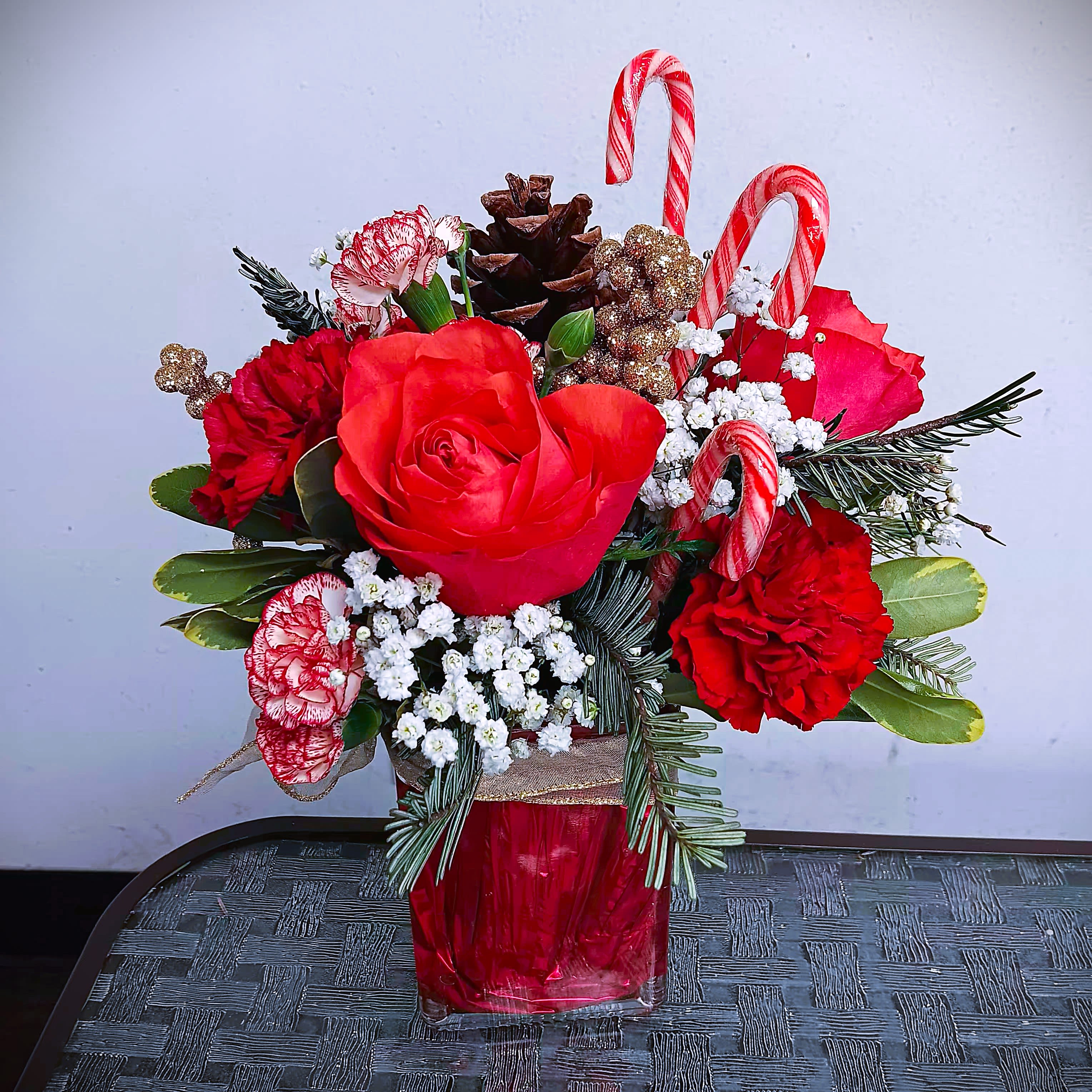 Rubies and Candy Canes - Fresh floral arrangement in rectangular glass vase with roses, carnations, holiday greens, and candy canes! We deliver.