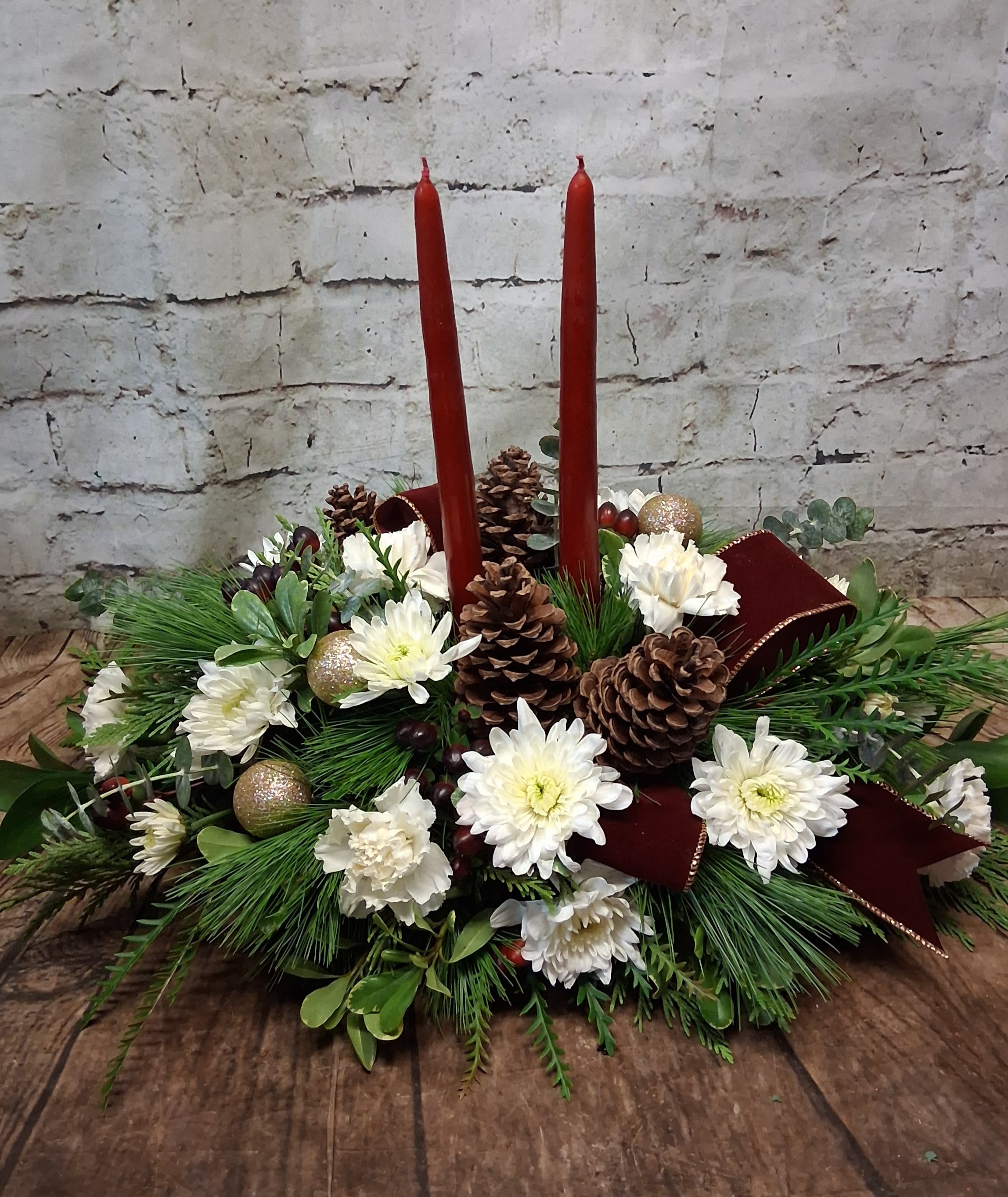 Season's Greeting Centerpiece  - A traditional long and low Centerpiece featuring taper candles, assorted fragrant evergreens, long lasting carnations, chrysanthemum and berries accented with pinecone and Christmas baubles. 