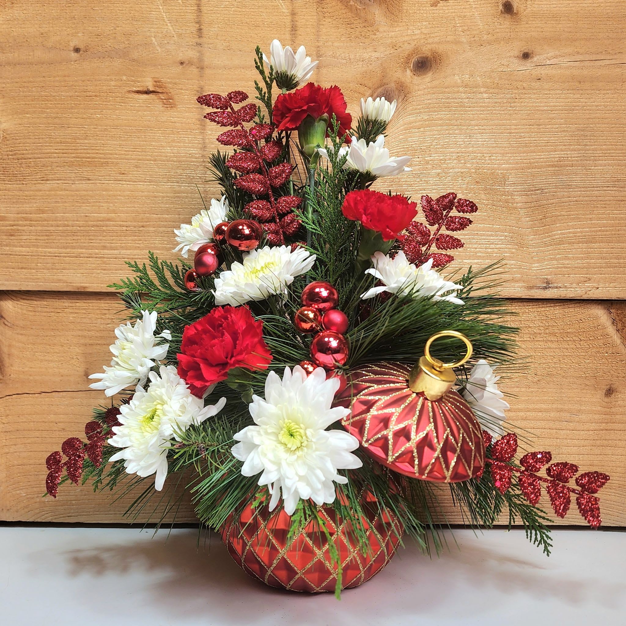Crimson Keepsake - Crimson Keepsake is an elegant way to spread holiday cheer this season! Glittering red accents are joined with red carnations and white pom-poms inside of an opulent red and gold ornament container to create a dazzling display, perfect for Christmas!  Dimensions approx. L 15" x H 16"