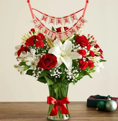 Fields of Europe Christmas with Banner - Here’s a gift blooming with holiday spirit. Inspired by the beauty of the European countryside, our best seller brings together radiant roses and lush white lilies in a glass vase wrapped in ribbon. Paired with our festive “Merry Christmas” banner, it’s a wonderful way to share your warmest wishes for the season.