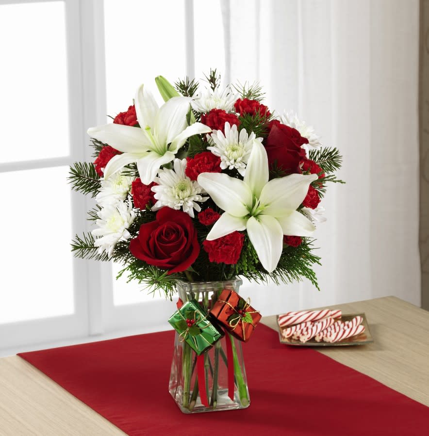  Our Joy Holiday Bouquet - The Joyous Holiday Bouquet is a seasonal sensation your special recipient will love. Rich red roses, carnations, and mini carnations are brought together with brilliant white Asiatic lilies and chrysanthemums accented with lush holiday greens to create an incredible fresh flower arrangement. Presented in a clear glass gathered square vase embellished with red ribbon at the neck dangling foil-wrapped present accents to give it a festive look, this holiday flower bouquet will make an excellent Christmas gift for your favorite friends, family or co-workers. 