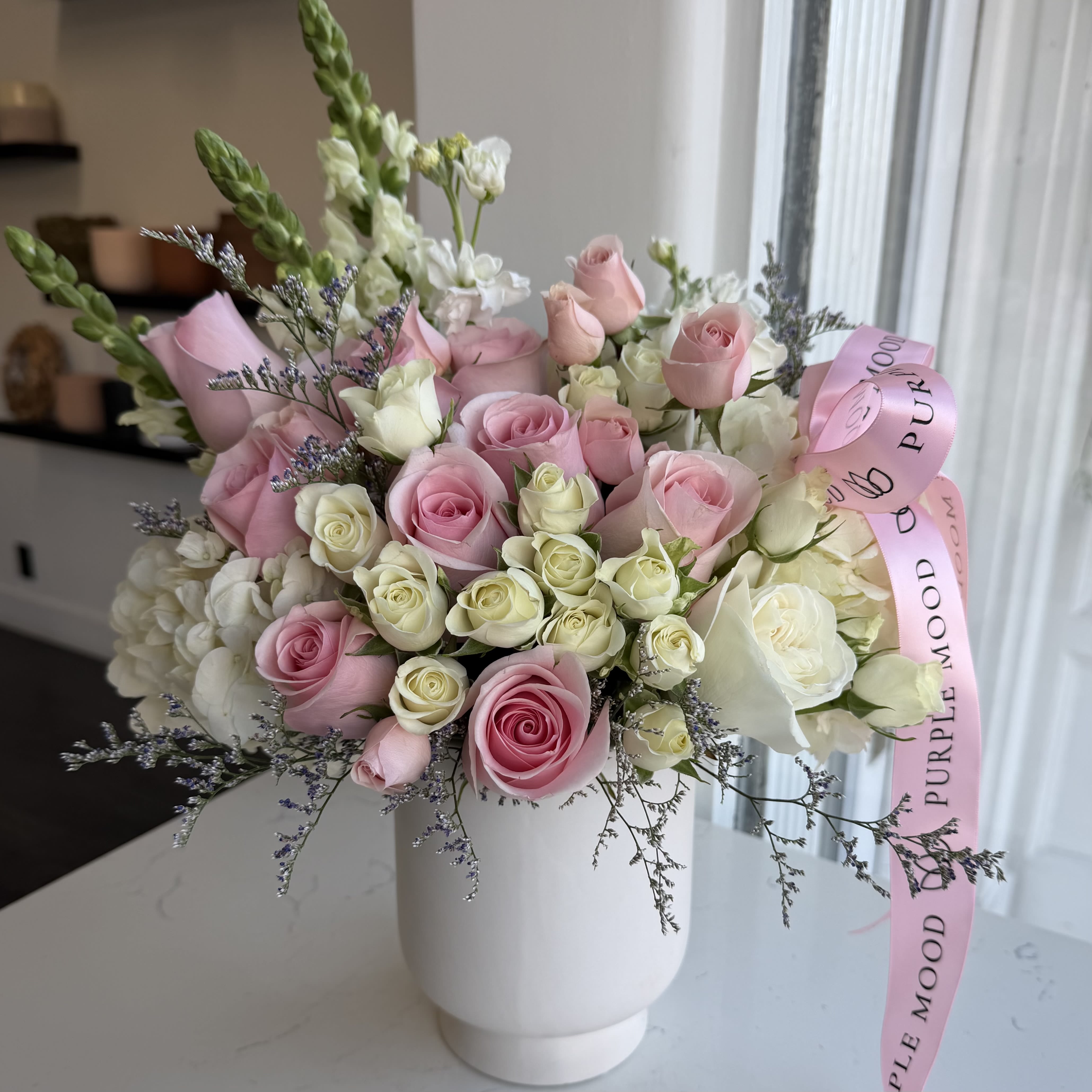 Enchanted Garden Vase - A soft pastel dream captured in a vase — romantic, airy, and full of charm. Shades of blush, lavender, and cream come together in a perfectly balanced design that feels both elegant and effortless. Finished with a satin ribbon, this arrangement brings a sense of calm beauty to any space or occasion.      •    Handcrafted in gentle pastel tones     •    Presented in a modern white vase     •    Finished with a soft satin ribbon     •    Perfect for birthdays, celebrations, or thoughtful gestures