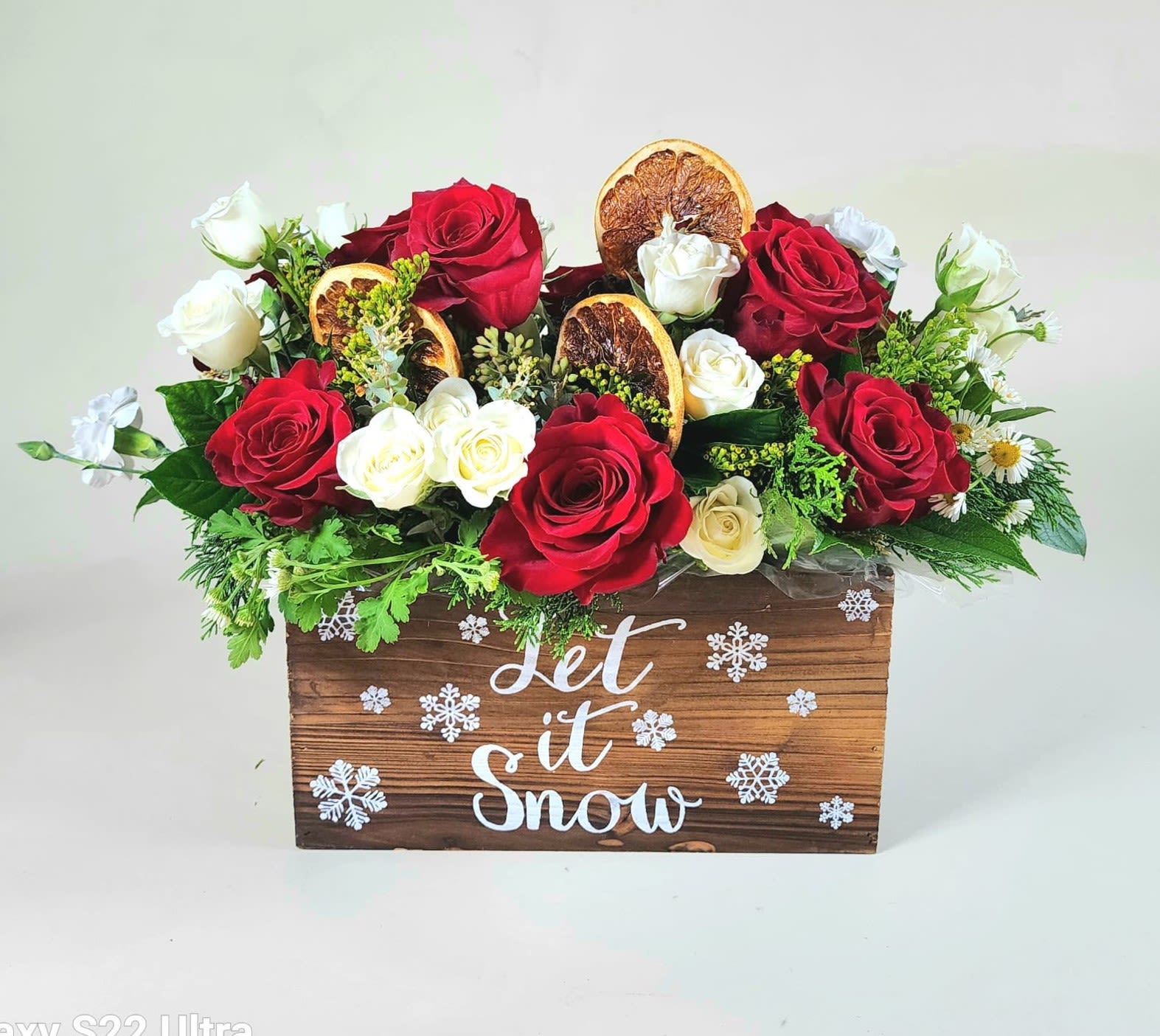 Winter Cheer Centerpiece – Holiday Red &amp; Ivory Rose Arrangement - A festive holiday centerpiece featuring rich red and soft ivory roses accented with seasonal greenery and dried orange slices. Designed in a rustic wooden box, this arrangement brings warmth, texture, and classic holiday charm to any space.  Perfect for dining tables, mantels, holiday gatherings, or seasonal gifting. Available for delivery in DeLand, Deltona, DeBary, Orange City, Lake Helen, Lake Mary, Sanford, Daytona Beach, and surrounding Central Florida areas. Flower varieties, greenery, and decorative accents may vary slightly based on availability while maintaining overall holiday style, fullness, and value.