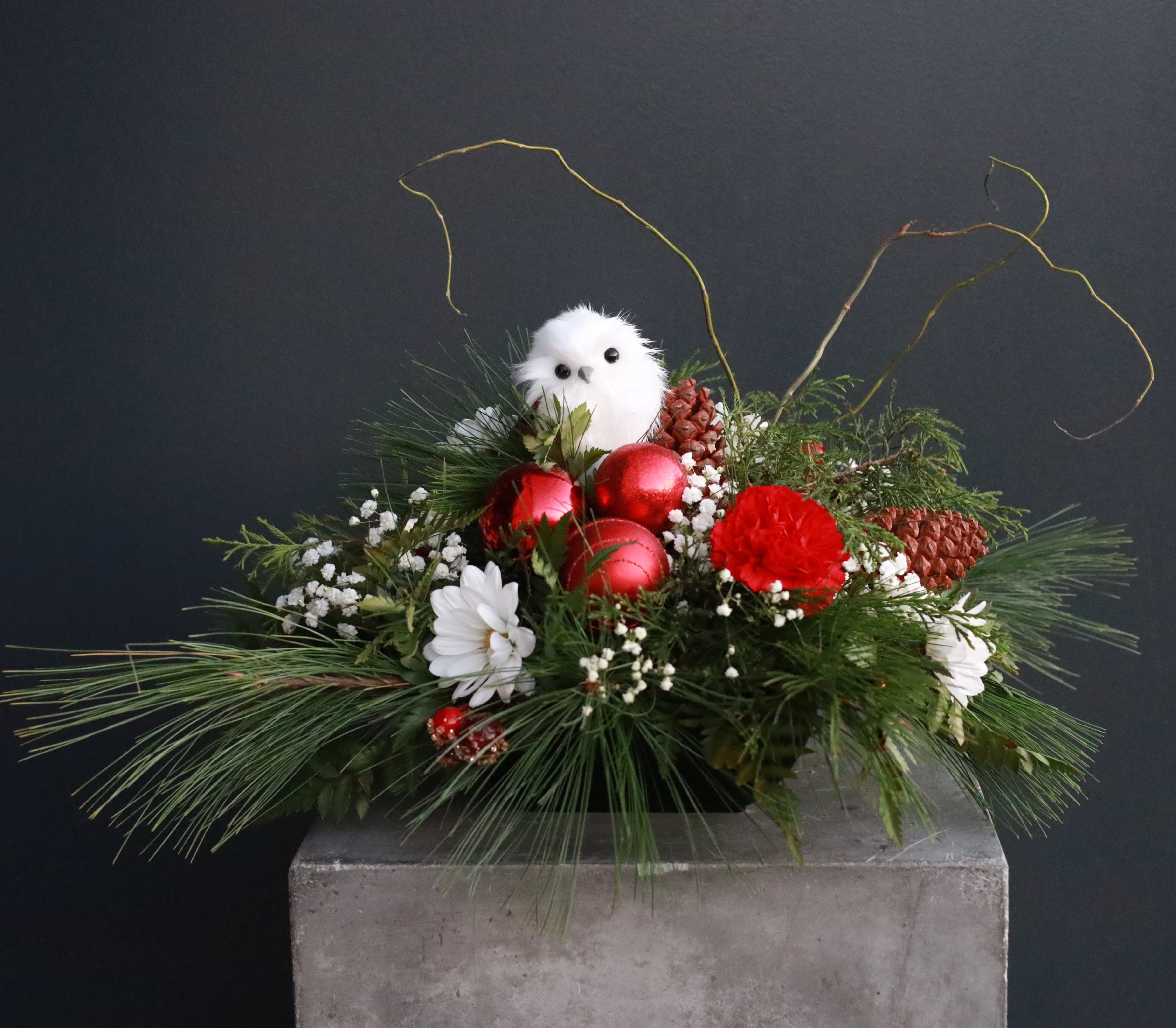 Snowy Owl - A lush arrangement with winter greenery, daisies, and baby's breath designed with touches of holiday decorations of red ornaments, pine cones, and a sweet snow owl.