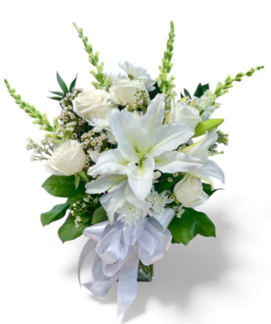 Eternal Memories Vase - This elegant sympathy arrangement is beautifully showcased in a 7" rectangular vase, conveying a sense of serenity and grace. Adorned with lush foliage, this bouquet features four exquisite white snapdragons that symbolize strength and resilience. Six pristine white roses express love and respect, while the Asiatic lily adds a touch of purity and remembrance. Complementing this harmonious arrangement are two delicate stems of white waxflower, representing enduring love and beauty. Together, these blossoms create a heartfelt tribute, offering comfort and solace to those in mourning.