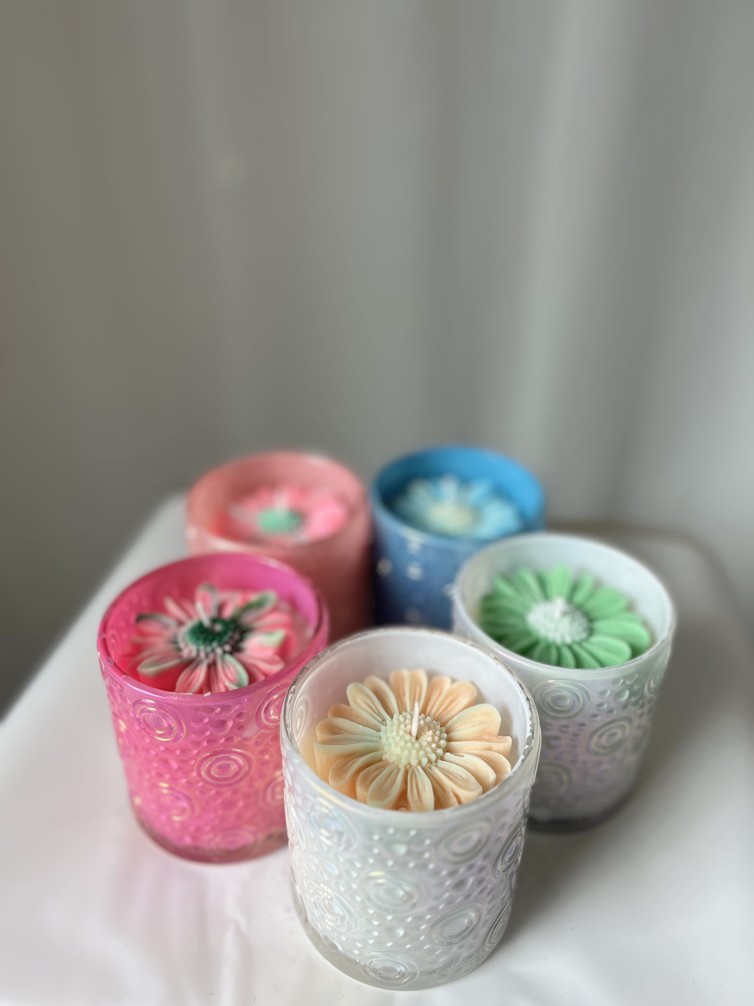 Daisy Bloom Candle - Add On - ONLY AVAILABLE FOR DELIVERY IF PURHASED WITH A FLORAL ARRANGEMENT OR PLANT*  A mini sized candle, but with a big scent! Made in a small glass votive container, and decorated with a wax daisy on top. Daisy scented. Multiple colors available, leave your preference in the instructions- if you have one. Aromagia©