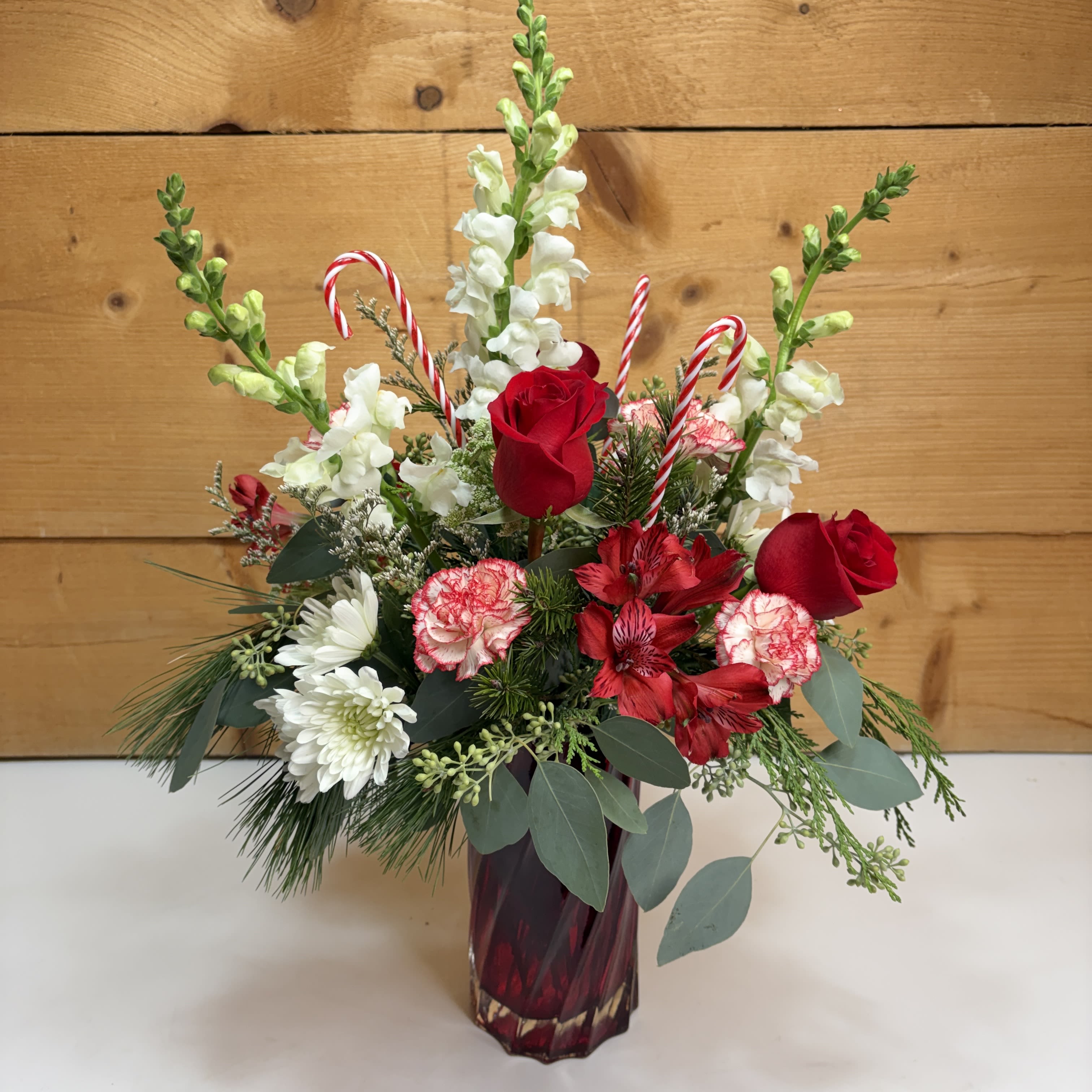 Peppermint &amp; Pine Bouquet - Celebrate the season with the timeless charm of our Peppermint &amp; Pine Bouquet. This festive arrangement blends crisp holiday reds and whites with fresh seasonal greenery for a look that feels both cozy and elegant. Designed with fragrant snapdragons, vibrant alstroemeria, classic roses, soft spray cushion mums, and textured carnations, each bloom is thoughtfully arranged to create depth and movement. Decorative candy canes add a playful peppermint twist, making this bouquet a perfect choice for holiday gifting, winter celebrations, or adding cheerful seasonal flair to any space.