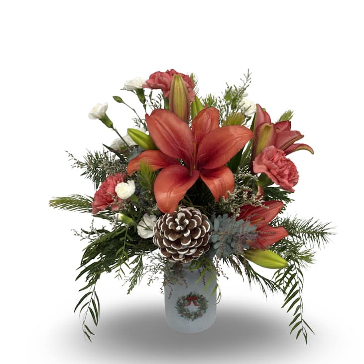 Merry Christmas Mason Jar - This festive arrangement features warm red lilies, soft seasonal blooms, lush greenery, and a frosted pinecone accent, all designed in a charming holiday mason jar. Measuring approximately 16 x 13 inches, it’s a cheerful and elegant way to add seasonal color and holiday spirit to any space.