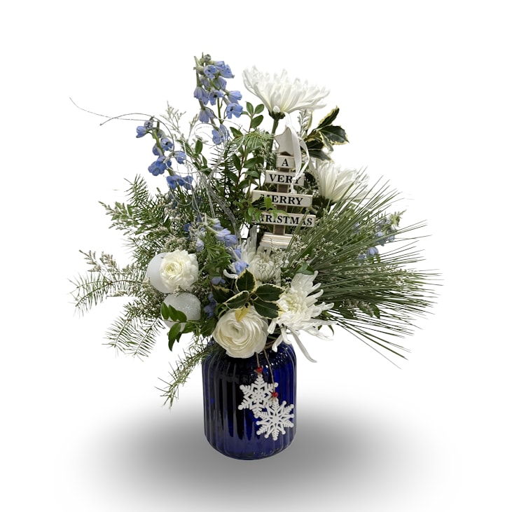 Blue Frost - This festive winter arrangement features crisp white blooms, soft blue accents, lush seasonal greenery, and a playful wooden ornament that reads “A Very Merry Christmas.” Designed in a deep blue glass vase with a snowflake charm, it offers a cool, elegant holiday feel. Measuring approximately 24 x 16 inches, this arrangement makes a cheerful and eye-catching centerpiece for celebrating the season.
