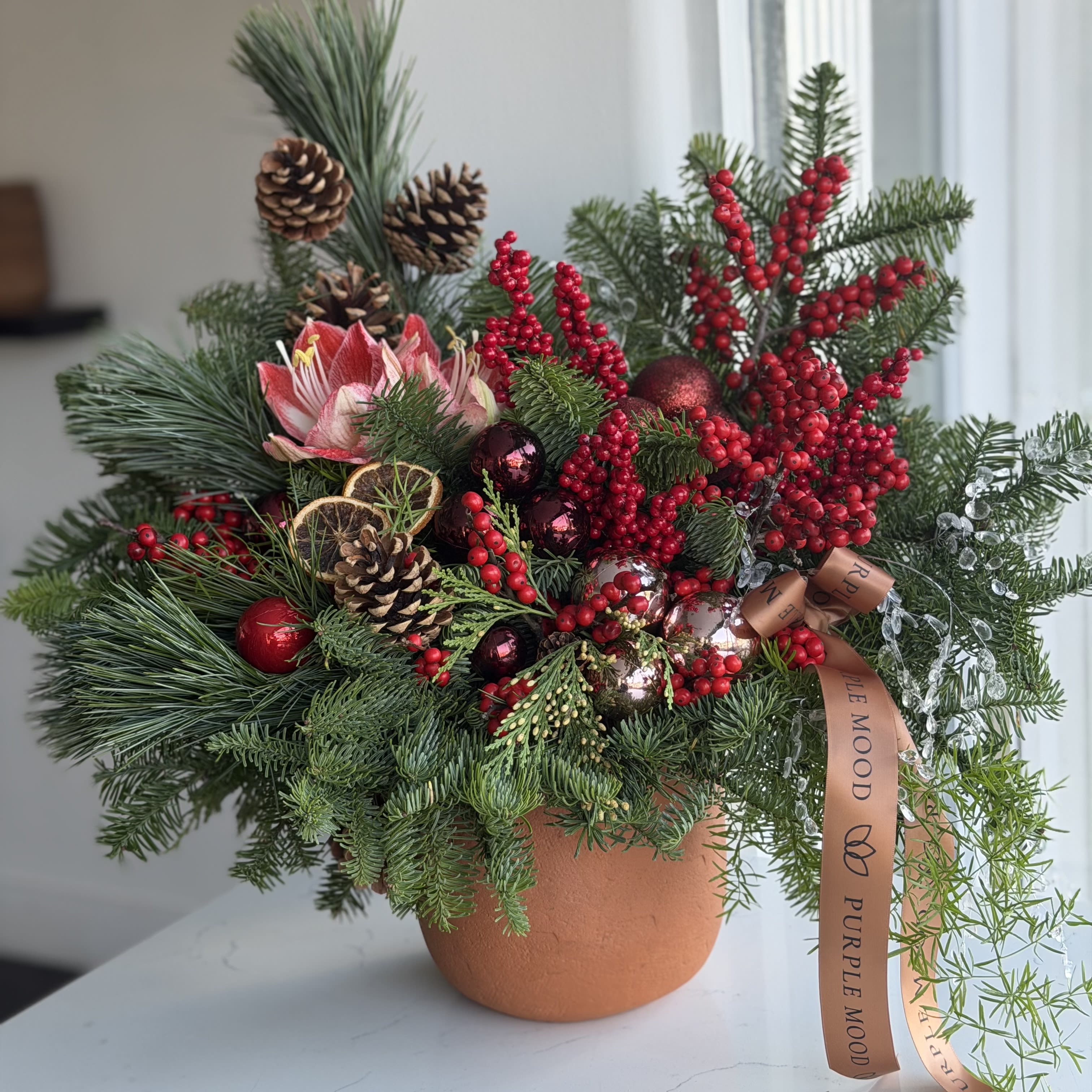Merry Berry Vase - A joyful and vibrant holiday arrangement designed to bring warmth and festive charm into any space. The Merry Berry Vase features a rich mix of winter evergreens, bright red berries, natural pinecones, glossy ornaments, and dried citrus slices for an aromatic seasonal touch. Styled in a warm terracotta vase, this piece blends rustic coziness with elegant holiday sparkle.  Perfect for gifting, holiday tablescapes, or adding a bold pop of Christmas red to your home. Same-day delivery available across Los Angeles. ️